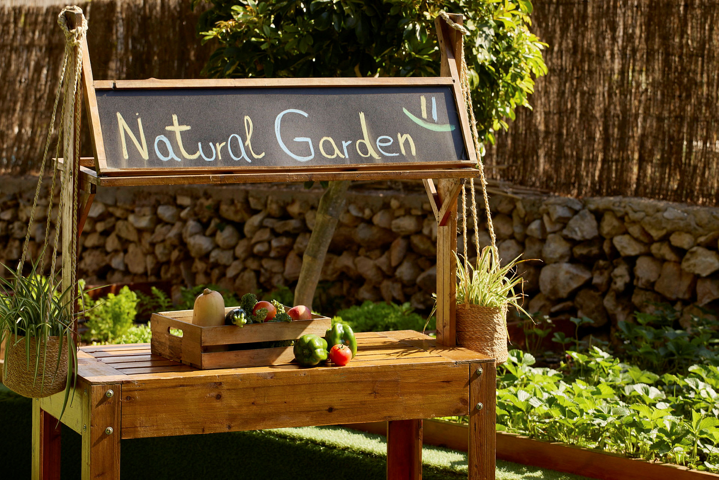 Trillebord i tre med skiltet "Natural Garden" og en kasse med grønnsaker, omgitt av hage og planter. (AI-generert tekst)