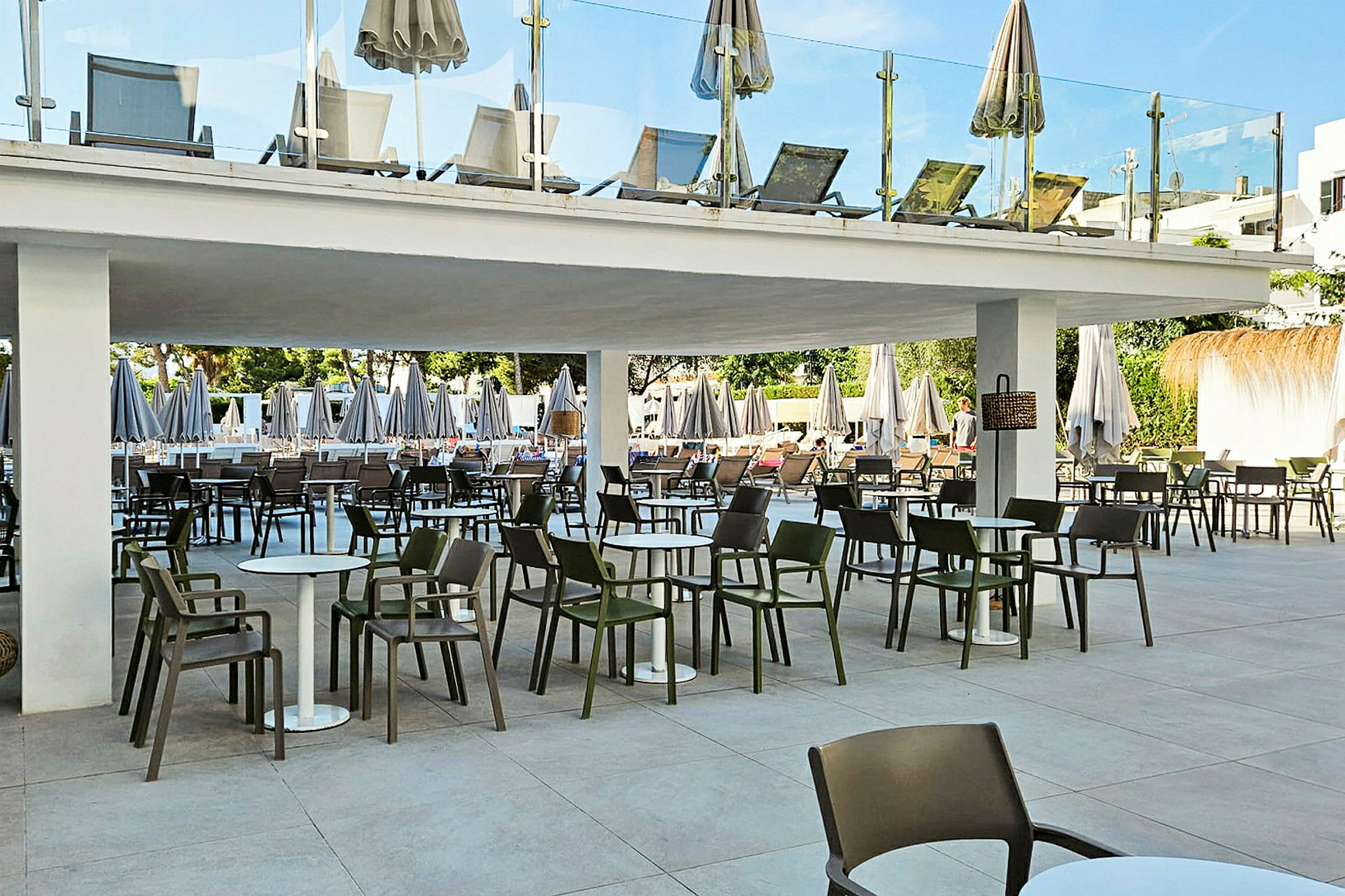 Bilde av en terrasse med bord og stoler under et tak, samt solsenger på en etasje ovenfor. (AI-generert tekst)
