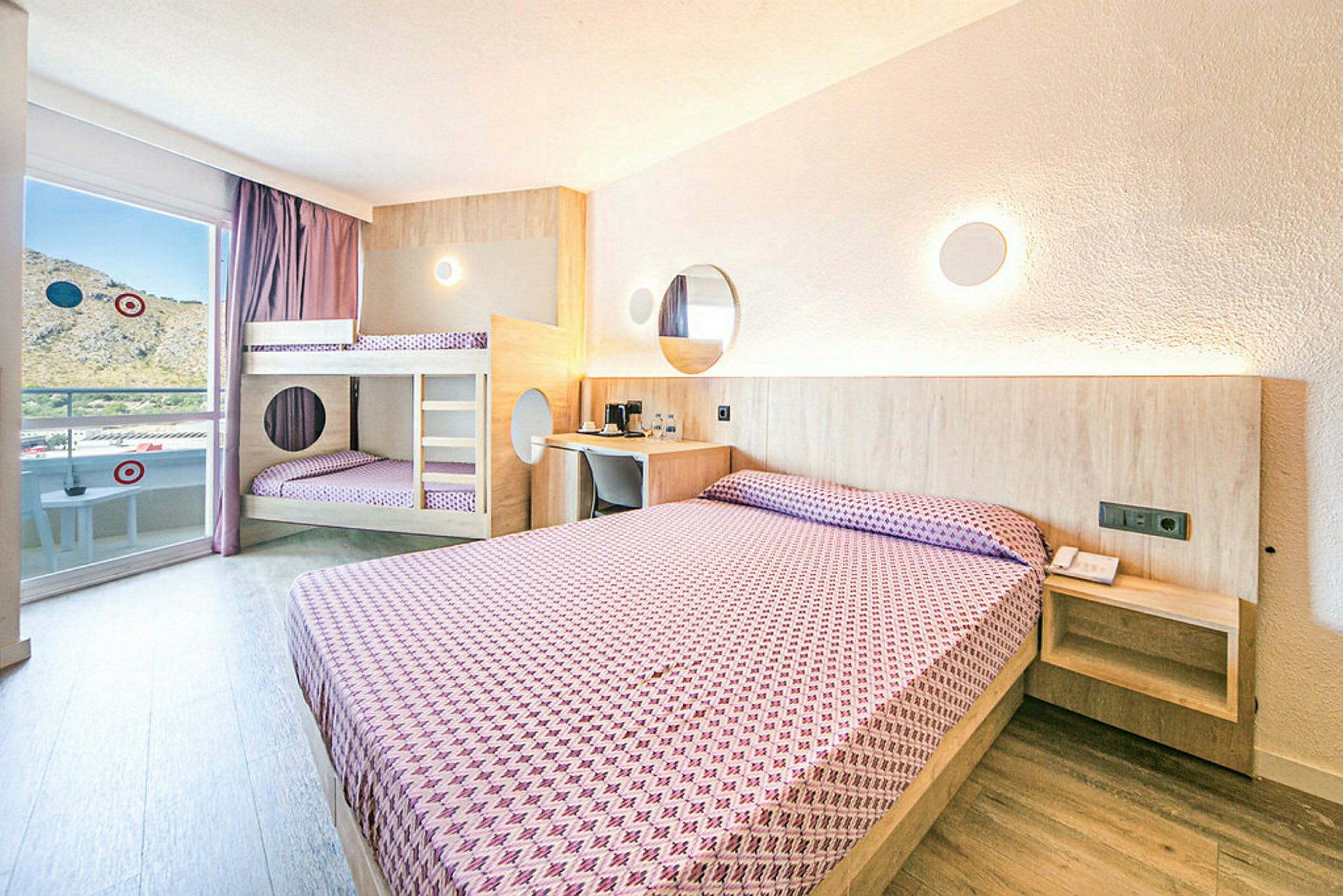 Et hotellrom med en dobbeltseng og en køyeseng, begge oppredd med lilla mønstrede sengetøy, lyse vegger og trefinish. (AI-generert tekst)