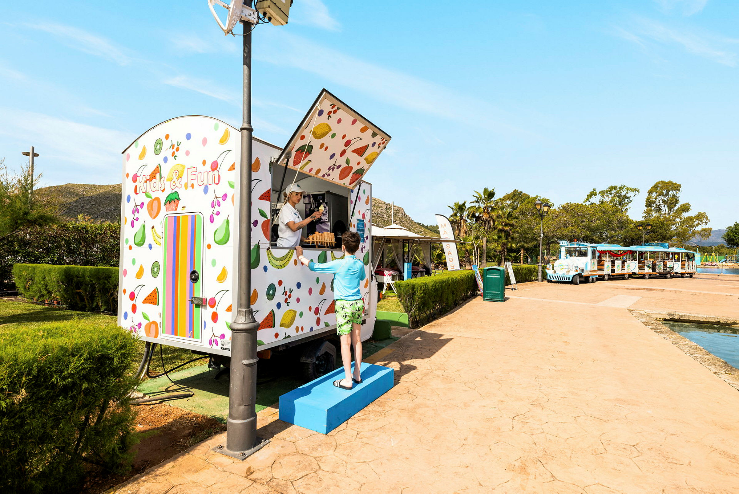 En fargerik kiosk med teksten "Kids & Fun". En person står foran og snakker med personalet i kiosken. (AI-generert tekst)