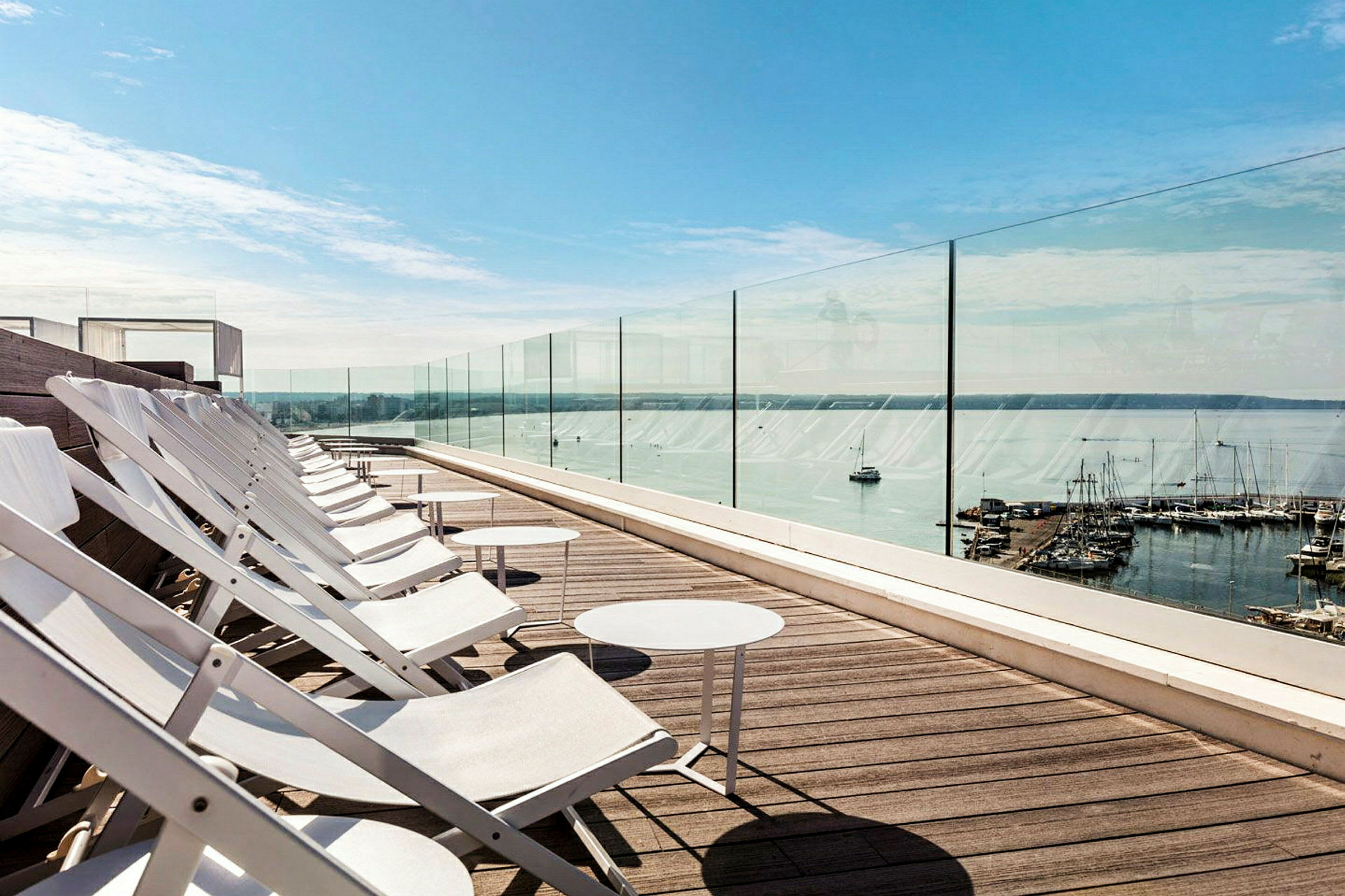 Solstoler på en takterrasse med utsikt over havet og en småbåthavn. (AI-generert tekst)