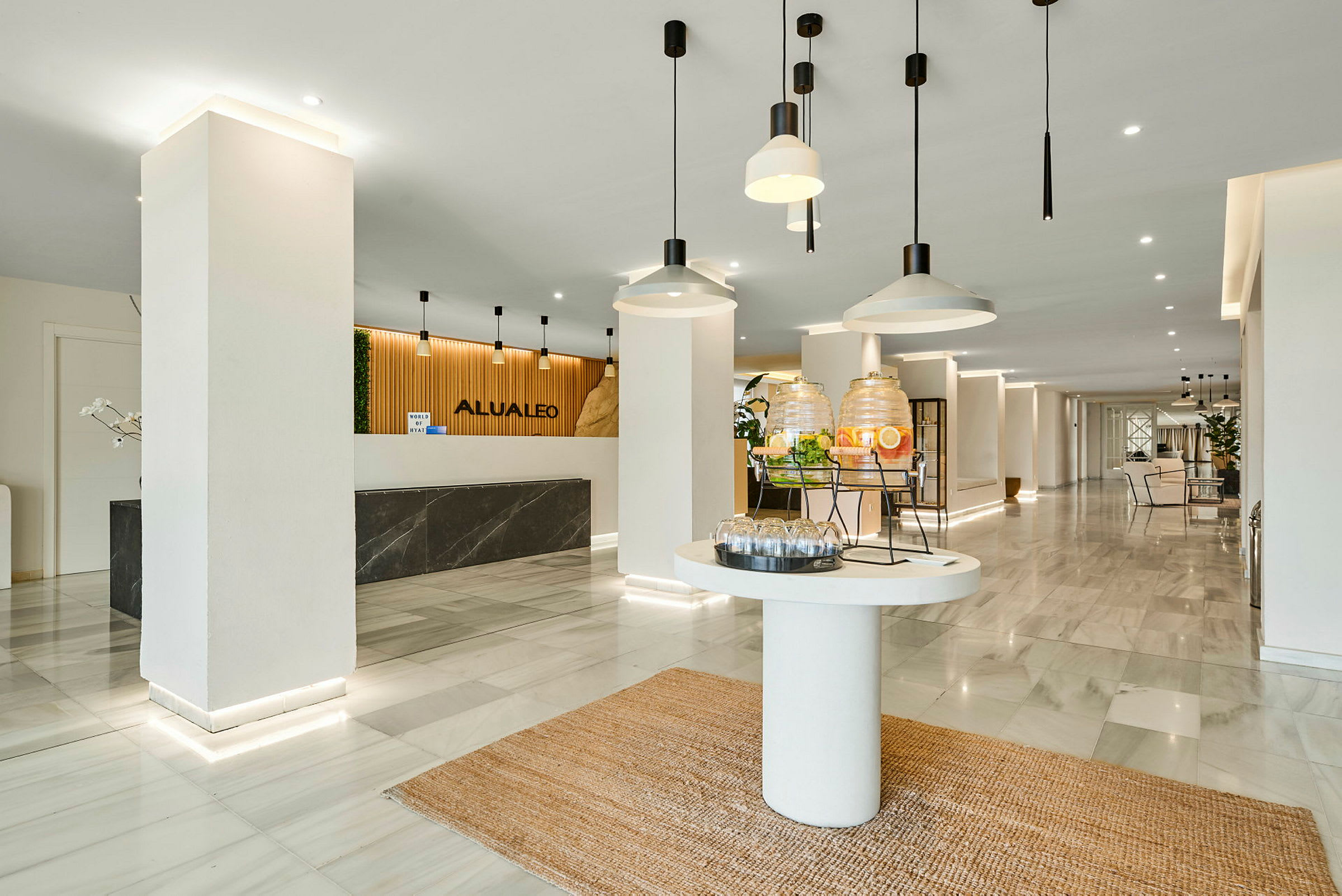 Hotellobby med resepsjonsdisk, en drikkestasjon og moderne interiør. (AI-generert tekst)