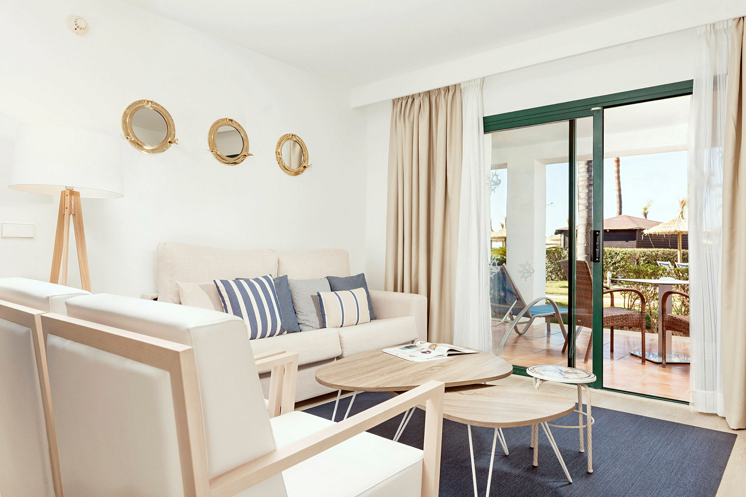 Lyst stue med sofa, puter og store vinduer med utsikt mot en terrasse. (AI-generert tekst)