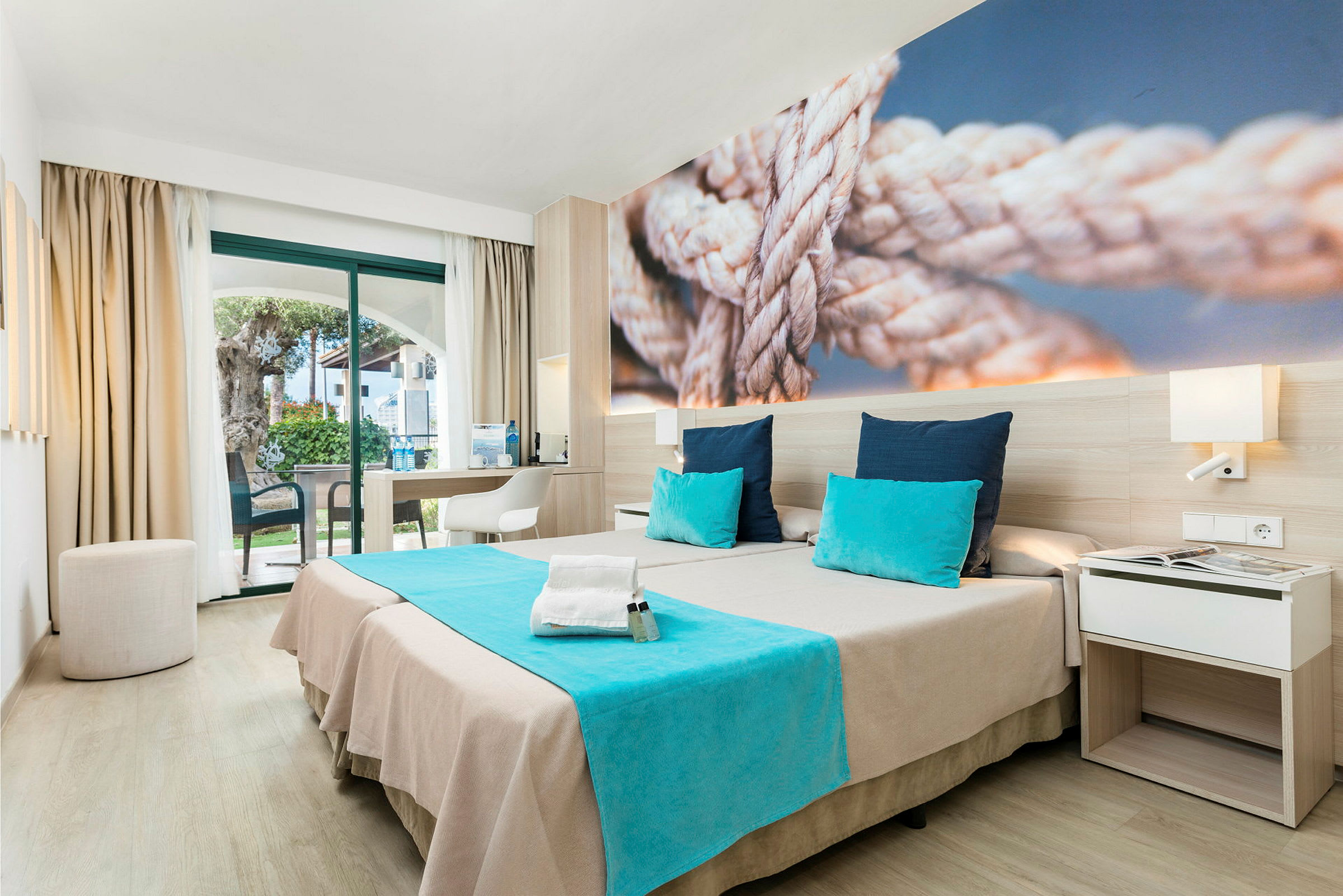 Moderne hotellrom med to senger, blå detaljer og et bilde av tau på veggen. (AI-generert tekst)
