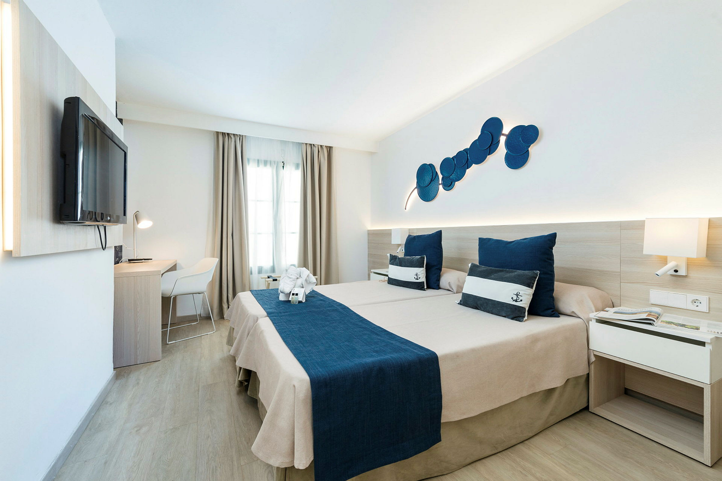 Hotellrom med to senger og maritimt tema, blått sengetøy og pynteputer. (AI-generert tekst)