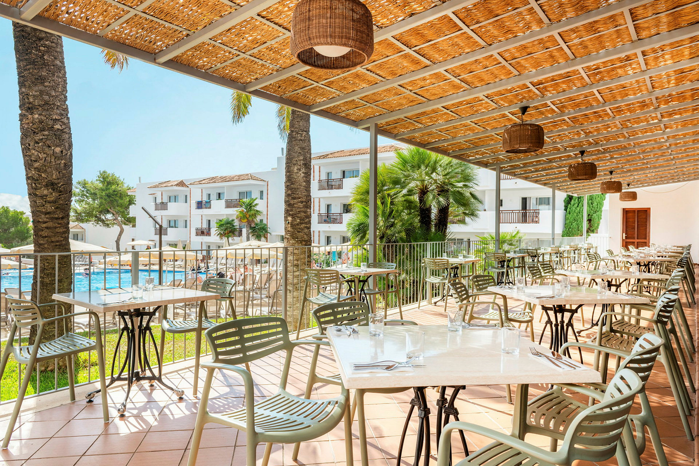Terrasse med bord og stoler, et basseng og hotellbygninger i bakgrunnen. (AI-generert tekst)
