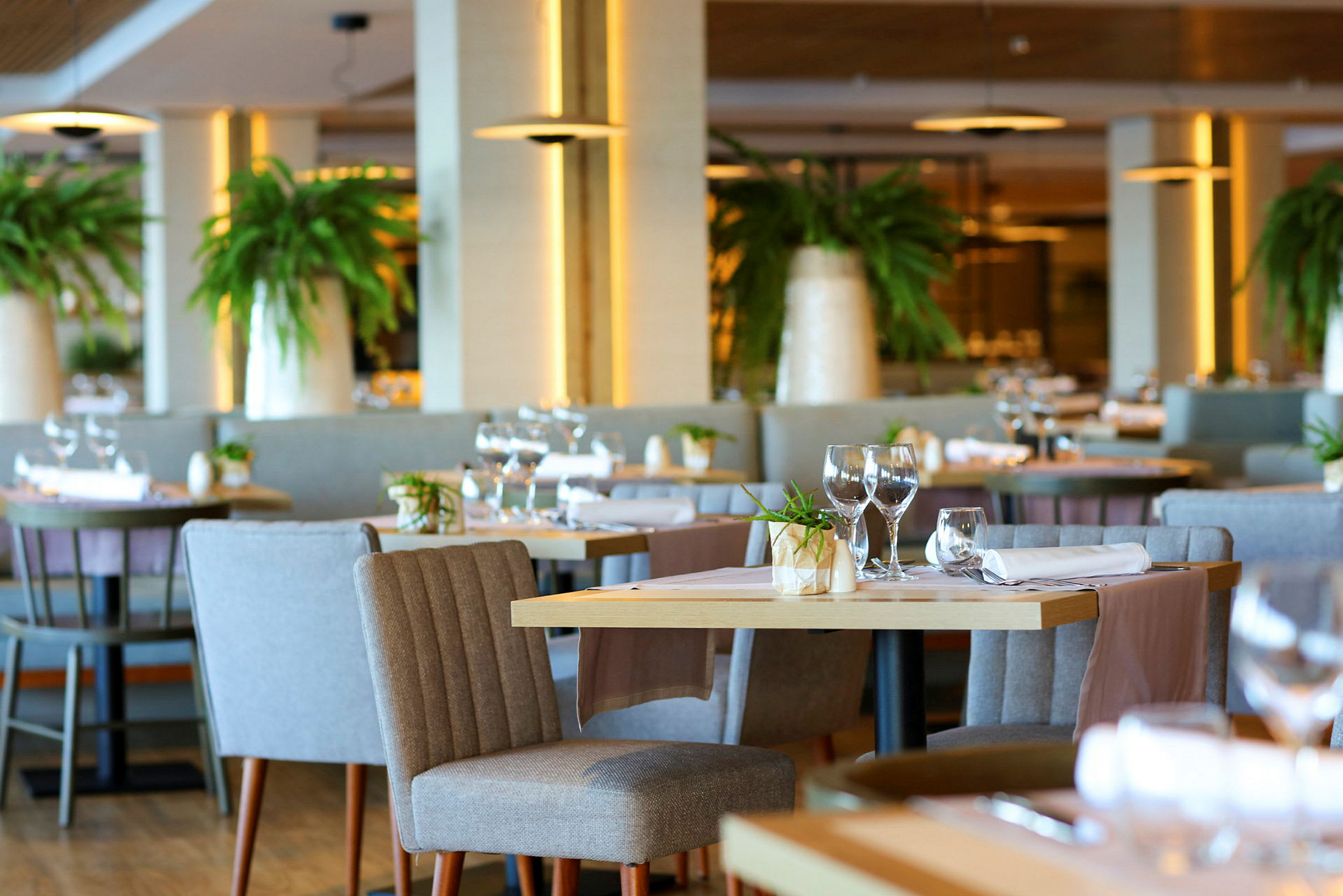 Interiør av en elegant restaurant med dekkede bord, komfortable stoler og grønne planter som dekorasjon. (AI-generert tekst)