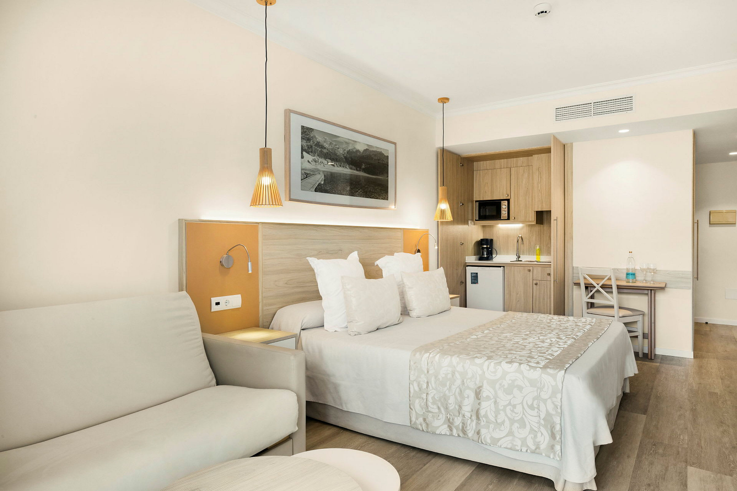 Et hotellrom med en dobbeltseng, sofa og et kjøkken i bakgrunnen. (AI-generert tekst)