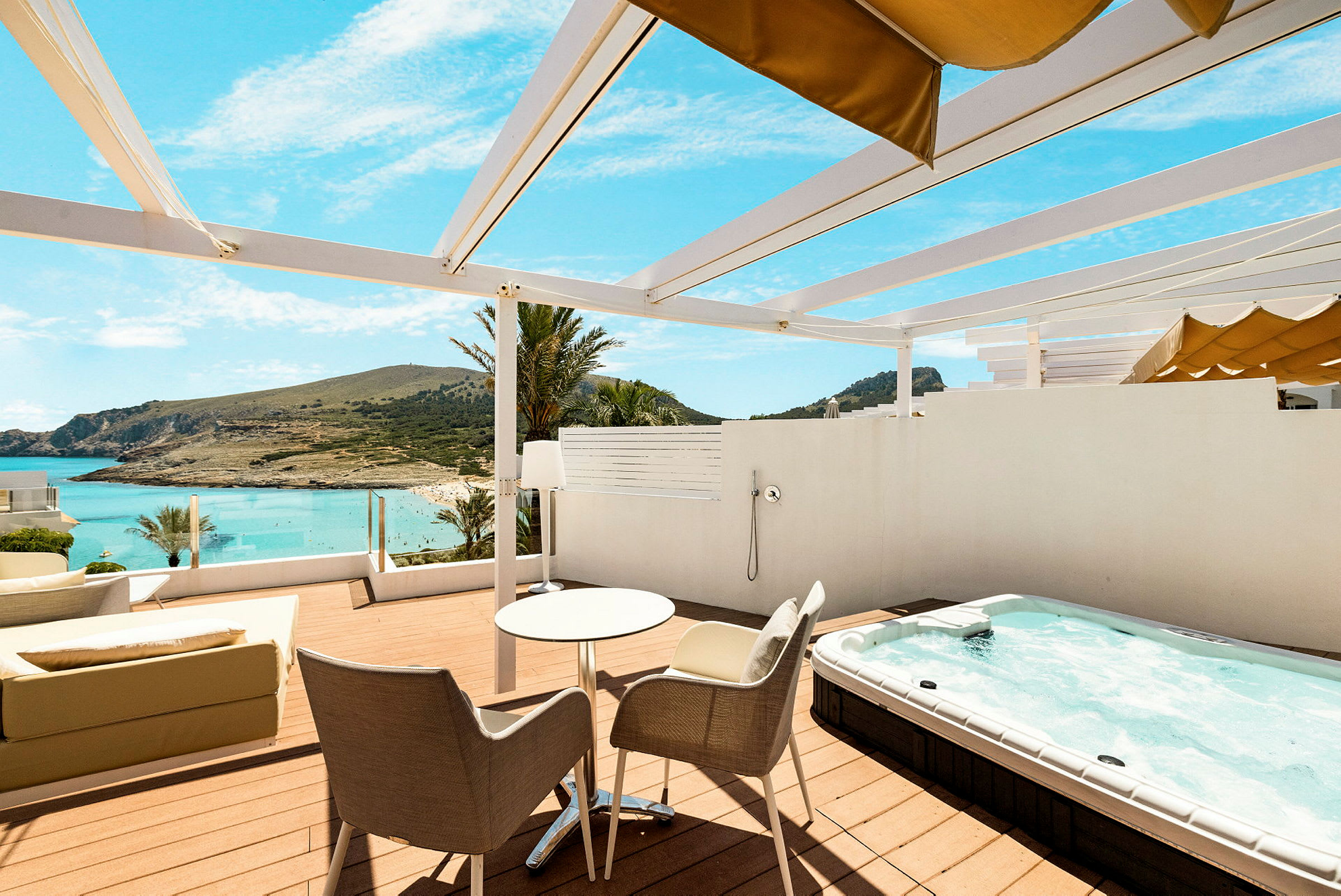 Terrasse med bord, stoler, boblebad og utsikt mot stranden og havet. (AI-generert tekst)