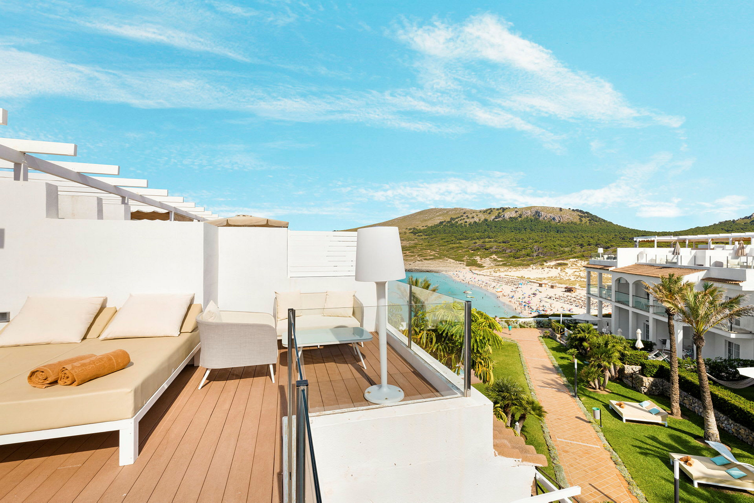 Utsikt over en terrasse med solsenger og stoler, med sandstrand og omkringliggende åser i bakgrunnen. (AI-generert tekst)