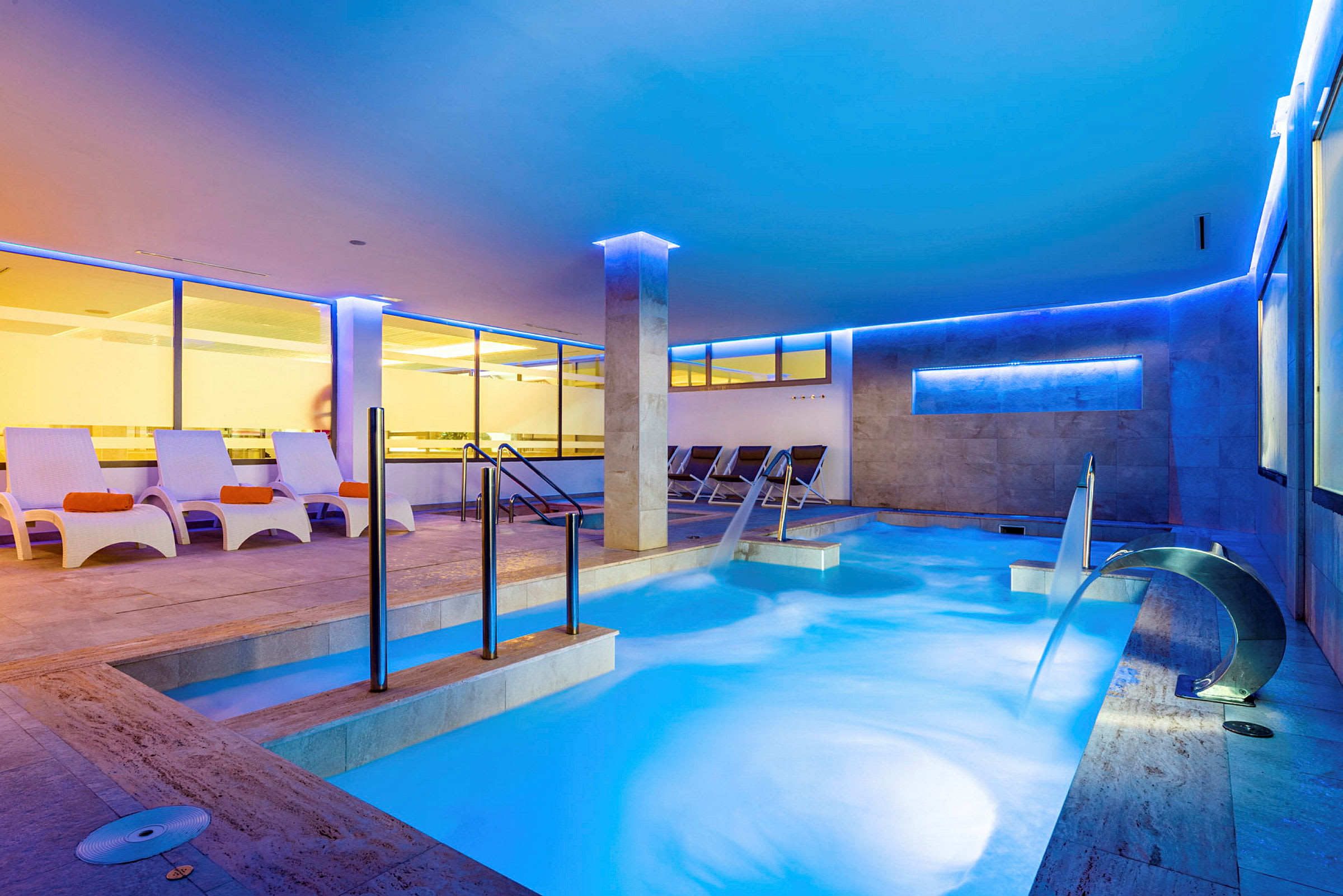 Innendørs basseng med sitteplasser og vannkaskade i et moderne opplyst spa. (AI-generert tekst)