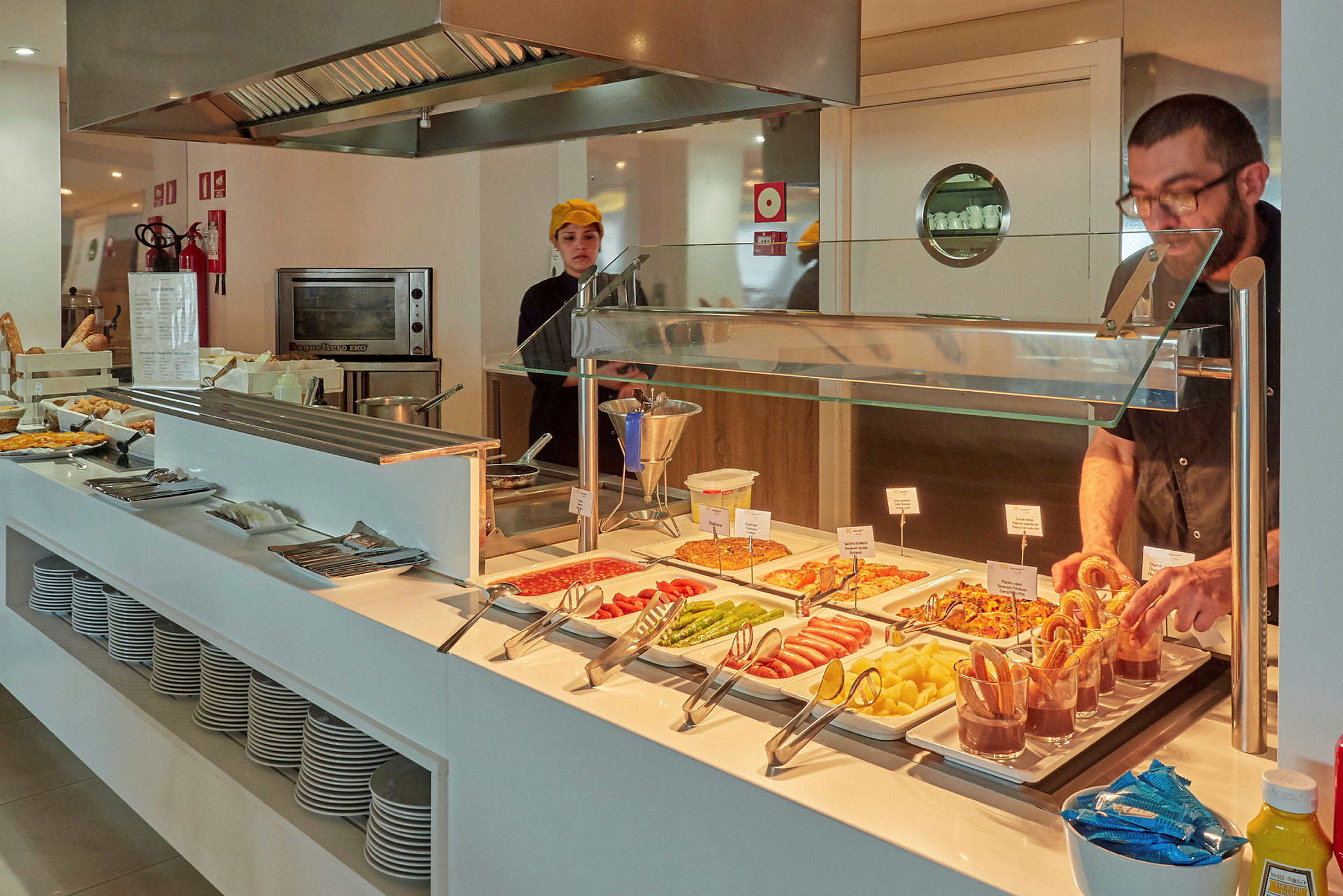 Buffébord med forskjellige retter, tallerkener og kjøkkenutstyr på en serveringsstasjon. (AI-generert tekst)