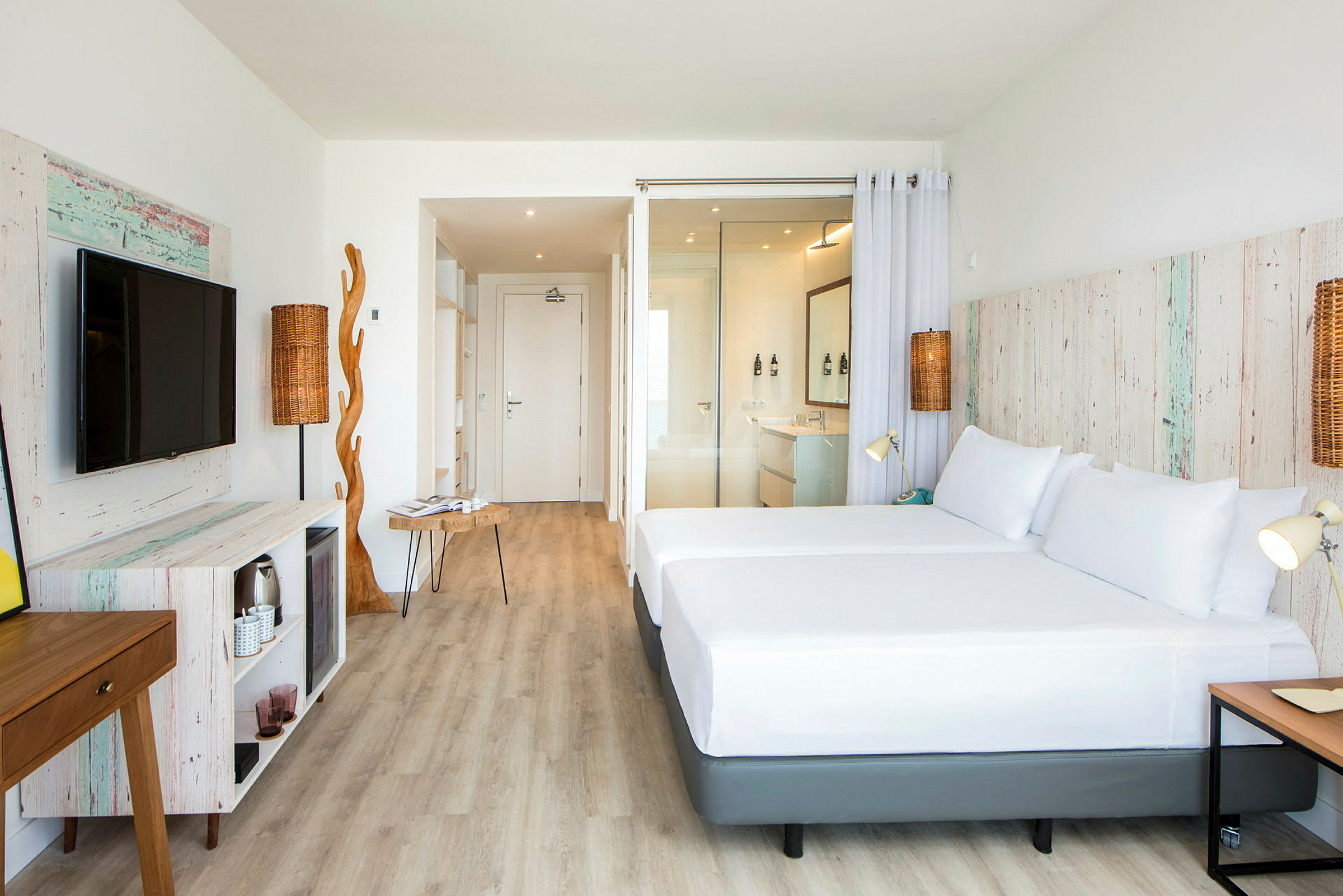 Et lyst hotellrom med trematerialer og moderne møbler. Rommet har en stor seng, en TV og en åpen løsning. (AI-generert tekst)