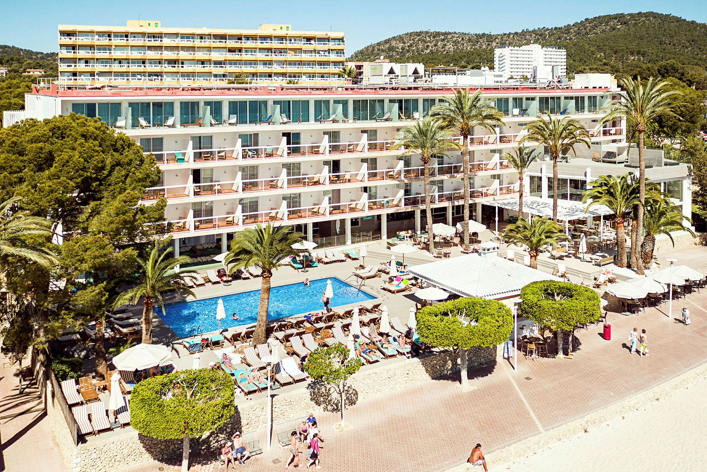 Et hotell ved stranden med basseng og solsenger omgitt av palmer. (AI-generert tekst)