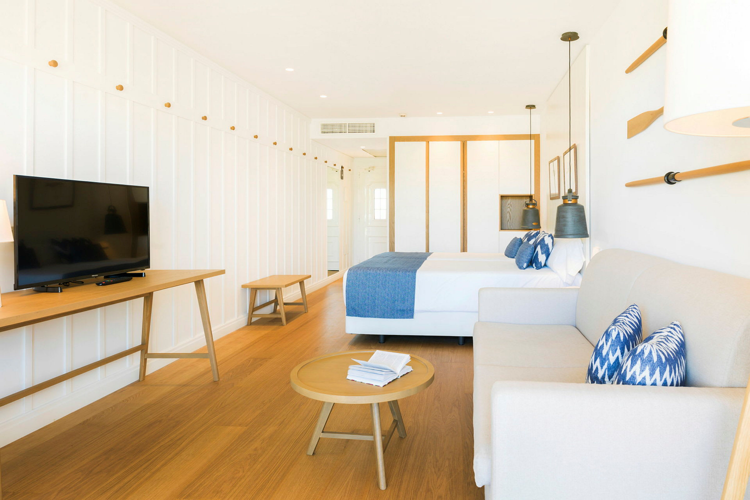 Et lyst innredet hotellrom med seng, sofa, salongbord og TV. (AI-generert tekst)