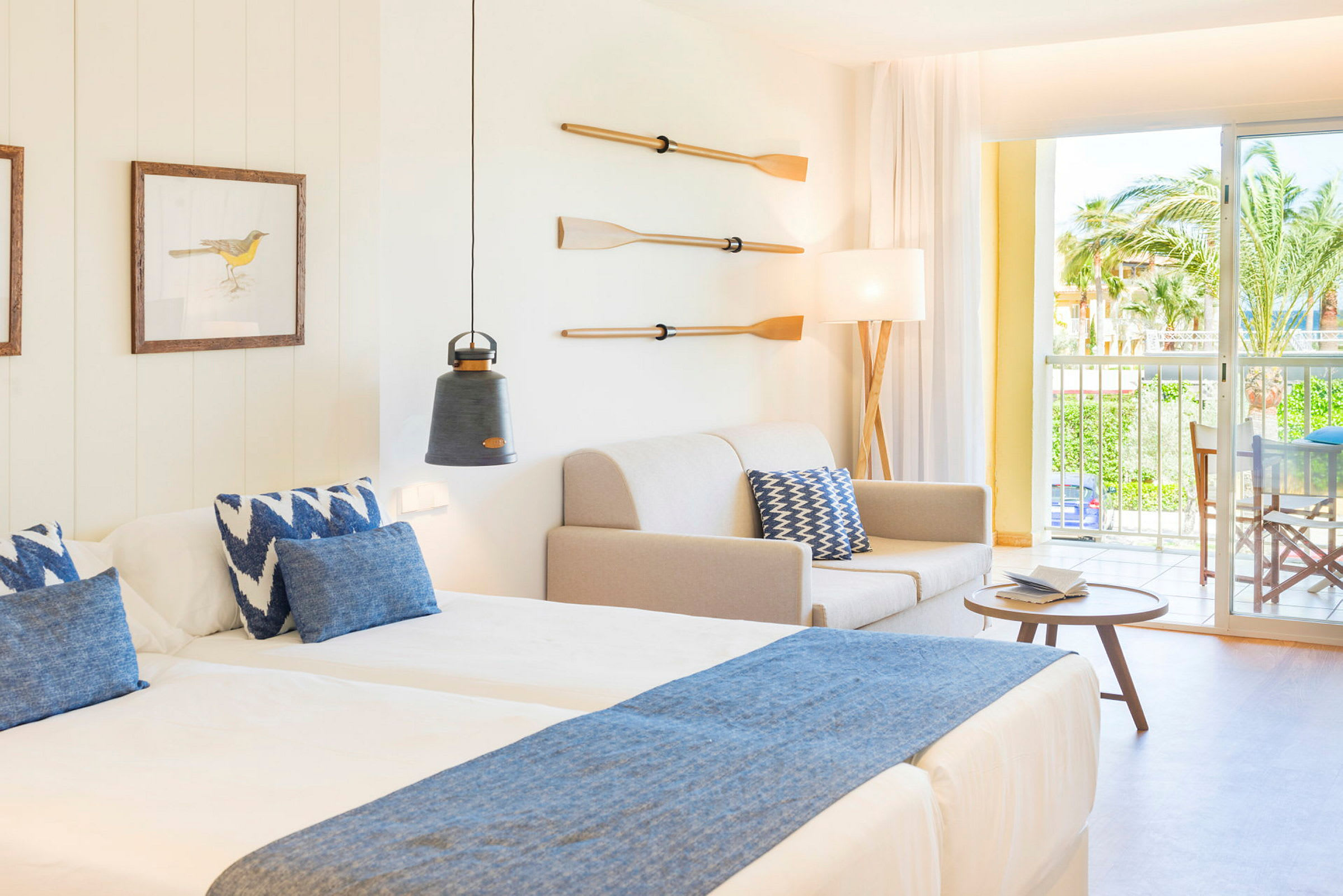 Et hotellrom med to senger, en sofa, en lampe, dekorerte årer på veggen og en balkong med utsikt. (AI-generert tekst)