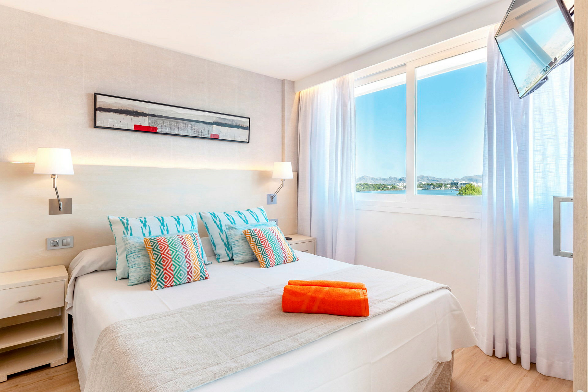 Hotellrom med belyst veggdekor, stor seng og utsikt over landskap gjennom vinduet. (AI-generert tekst)
