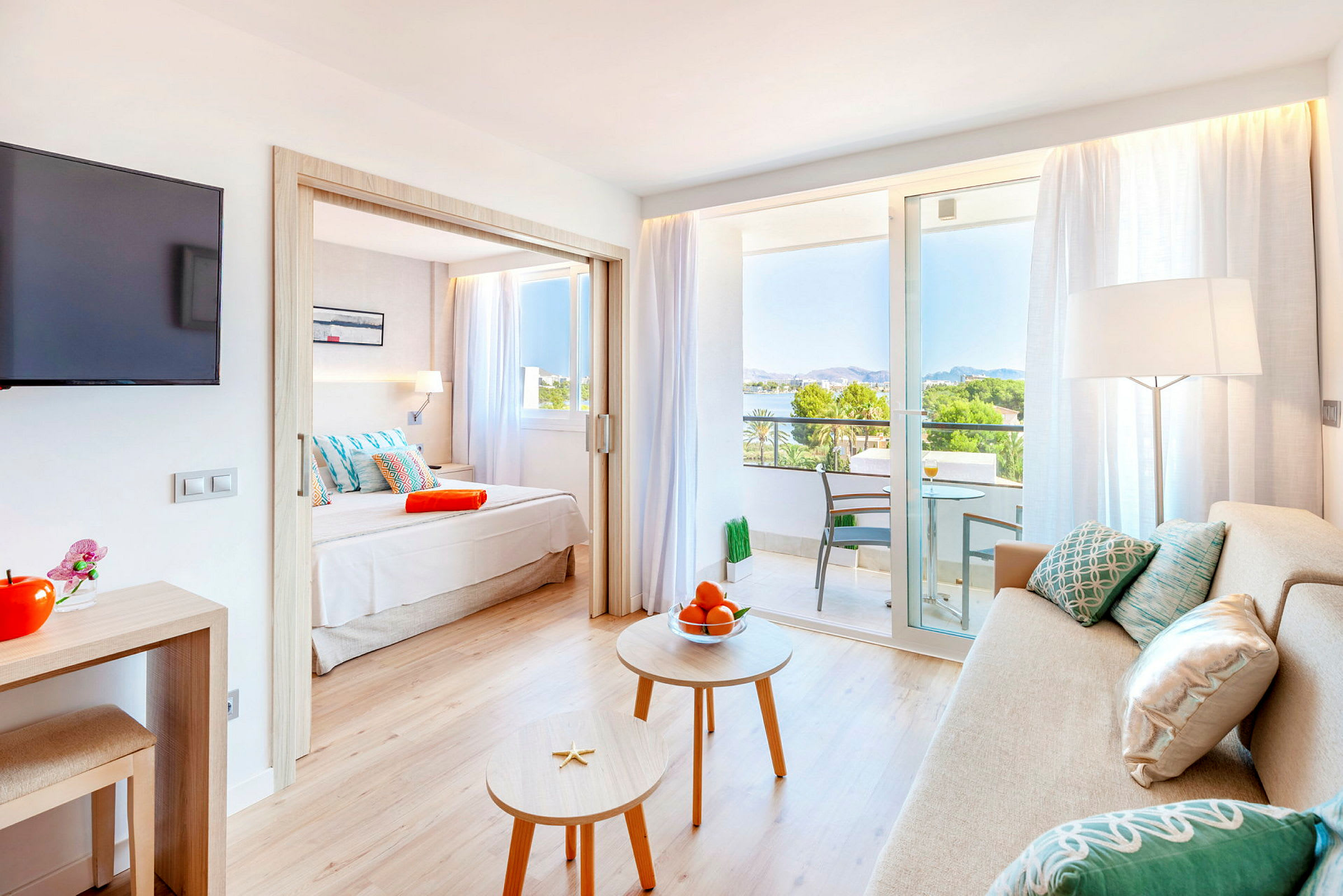 Interiør av et hotellrom med sofa, bord, en seng og en balkong med utsikt. (AI-generert tekst)