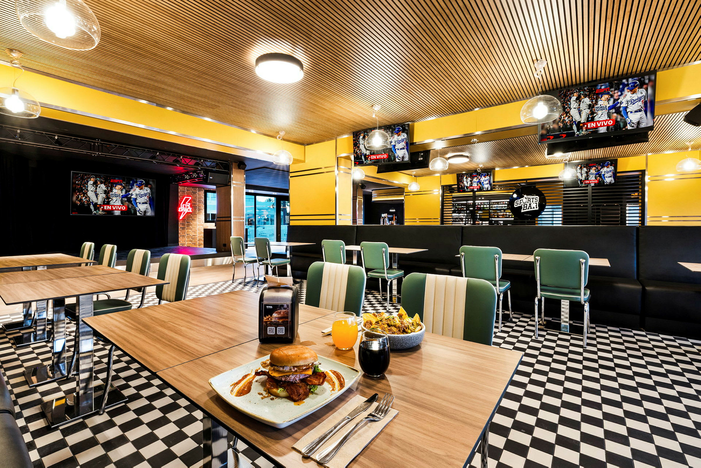 Interiør av en restaurant med bord og stoler, en tallerken med hamburger og drikke på et bord i forgrunnen. (AI-generert tekst)