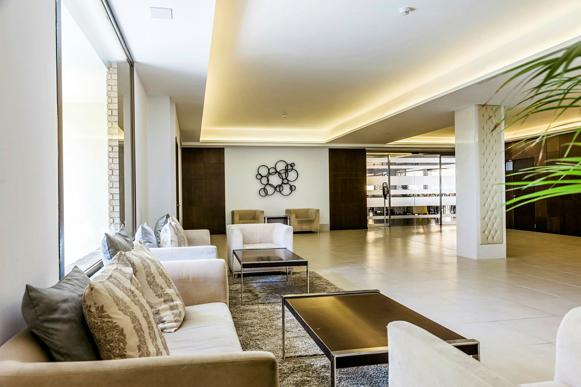 En moderne lobby med komfortable sofaer, bord og en dekorativ veggdetalj. Store vinduer og lys innredning. (AI-generert tekst)