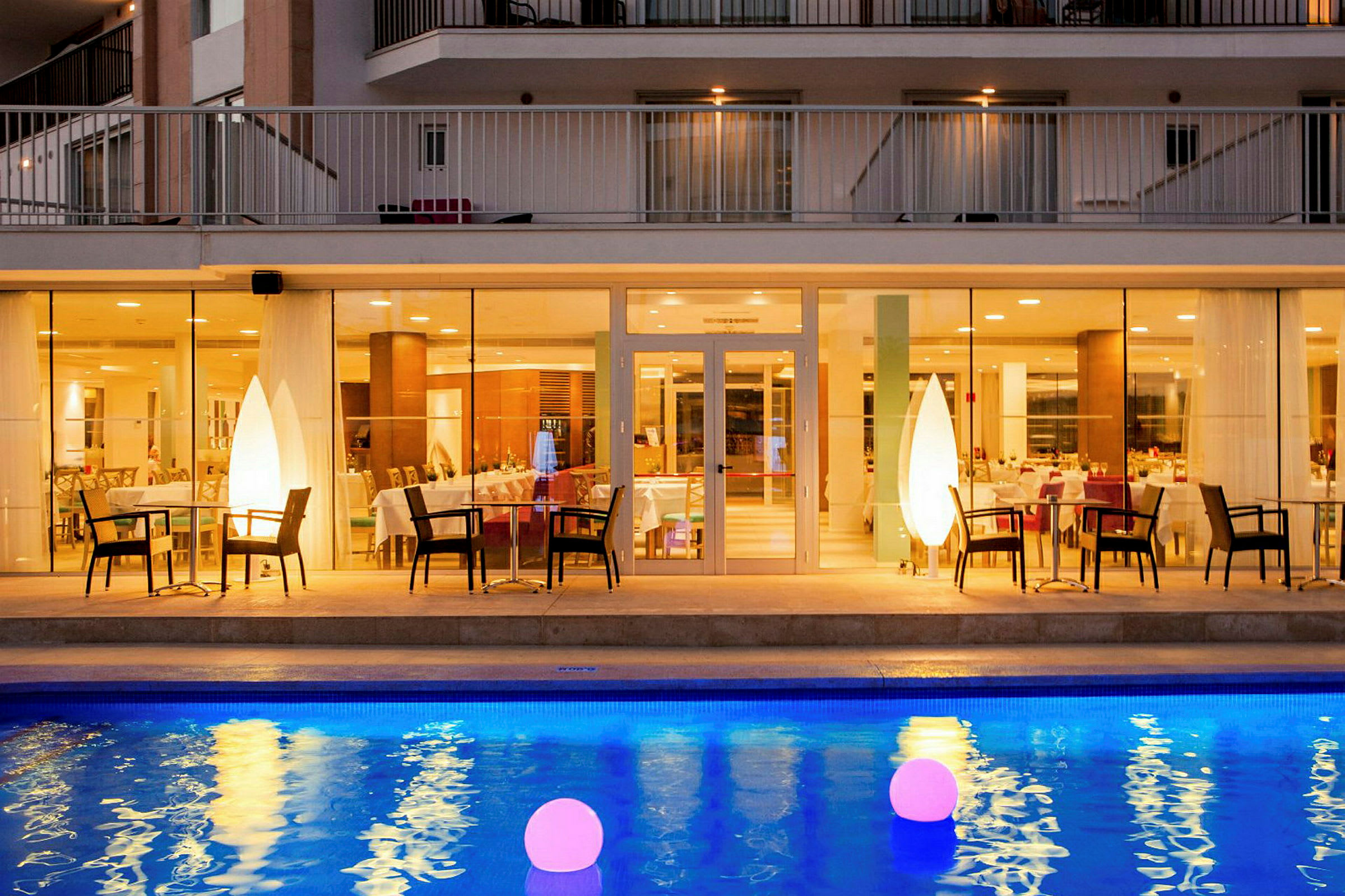 Hotellrestaurant med opplyst basseng i forgrunnen. (AI-generert tekst)