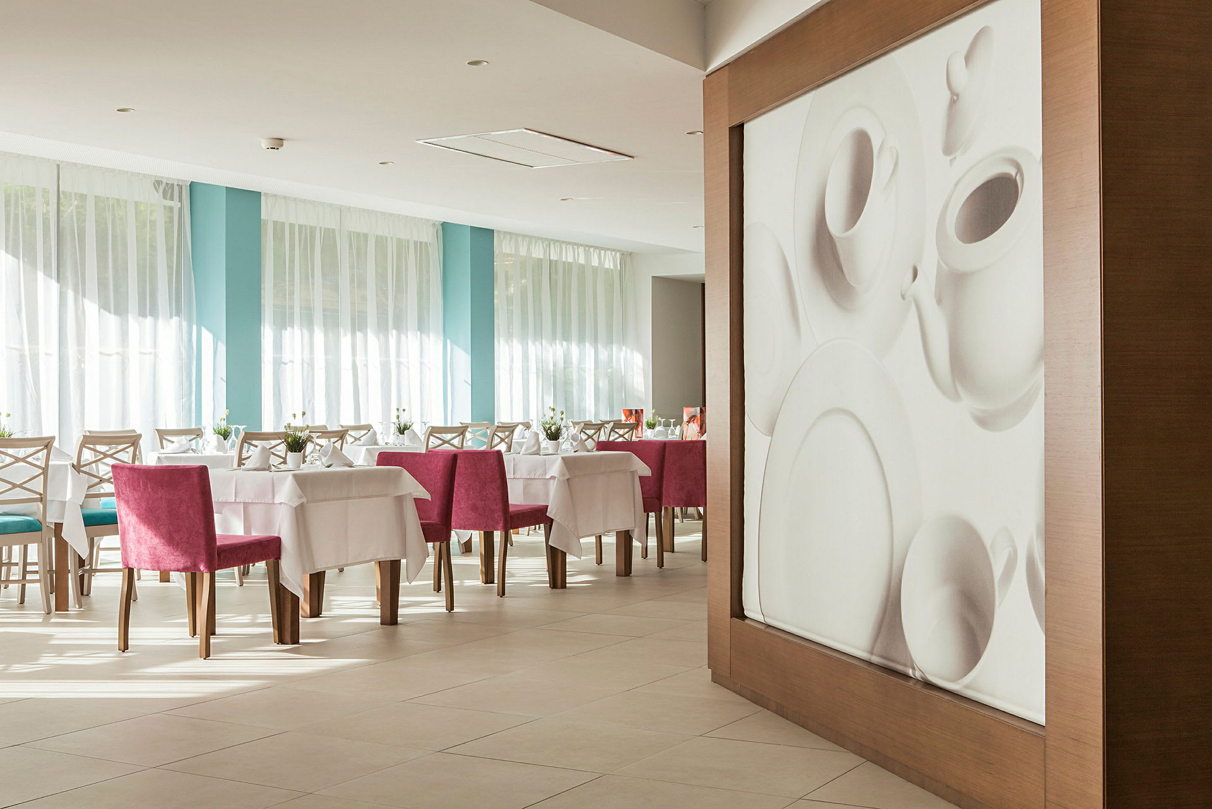 Interiør av en restaurant med dekkede bord og rosa stoler, samt en veggdekorasjon som forestiller porselen. (AI-generert tekst)