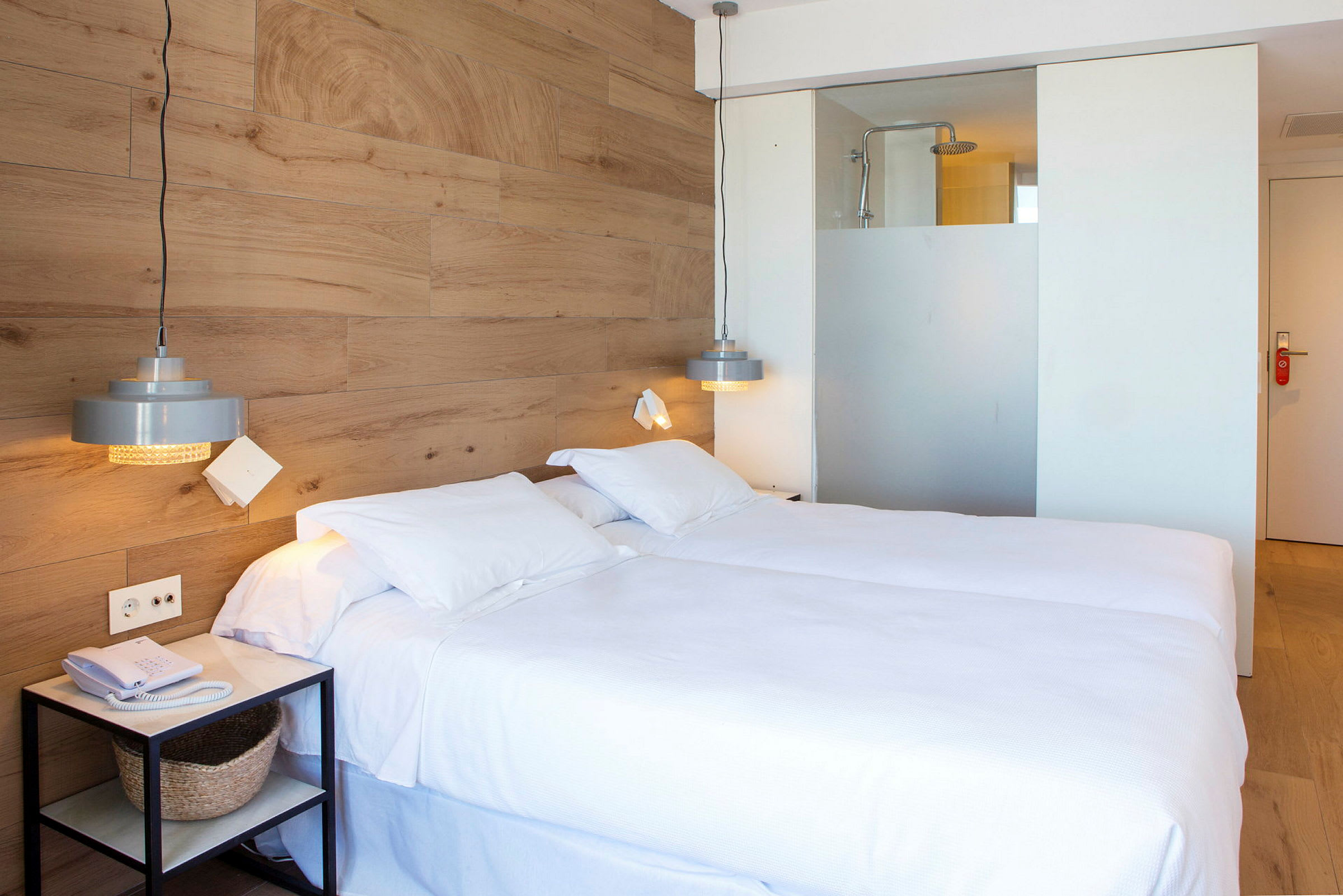 Hotellrom med en dobbeltseng, trevegg og en dusjdel synlig bak en glassvegg. (AI-generert tekst)