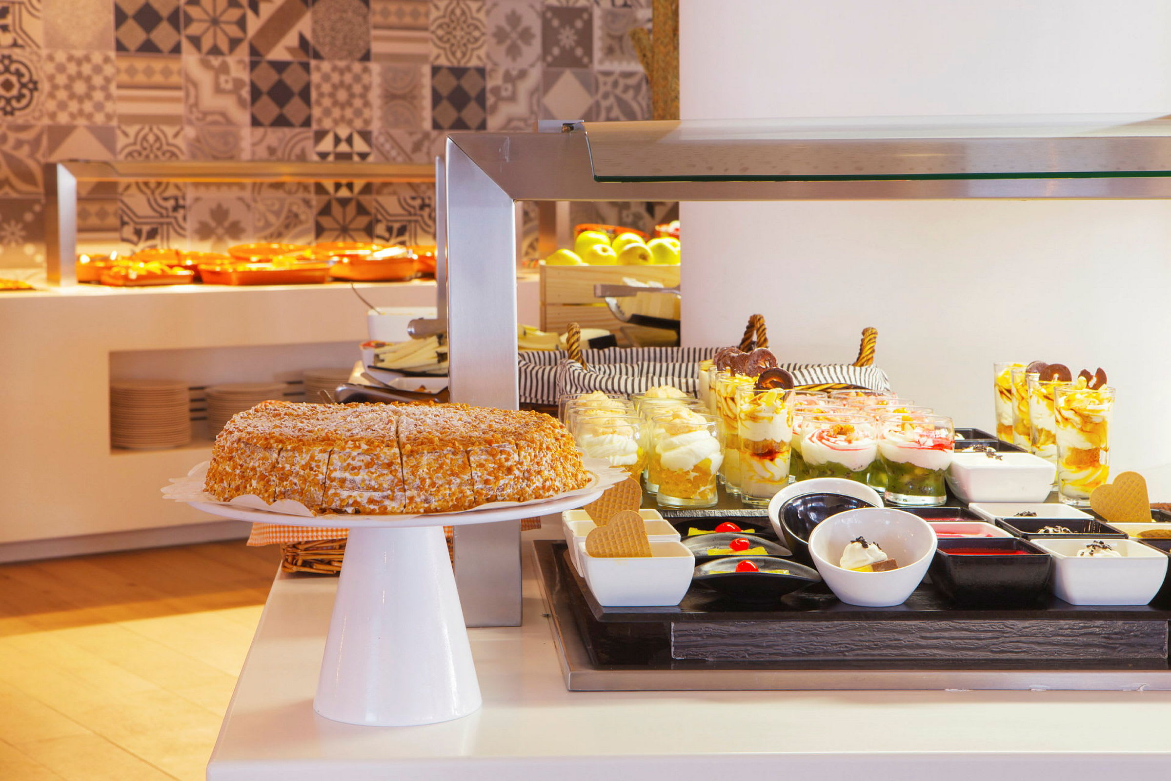 En buffet med desserter, inkludert en kake, glass med desserter og små skåler med tilbehør. (AI-generert tekst)