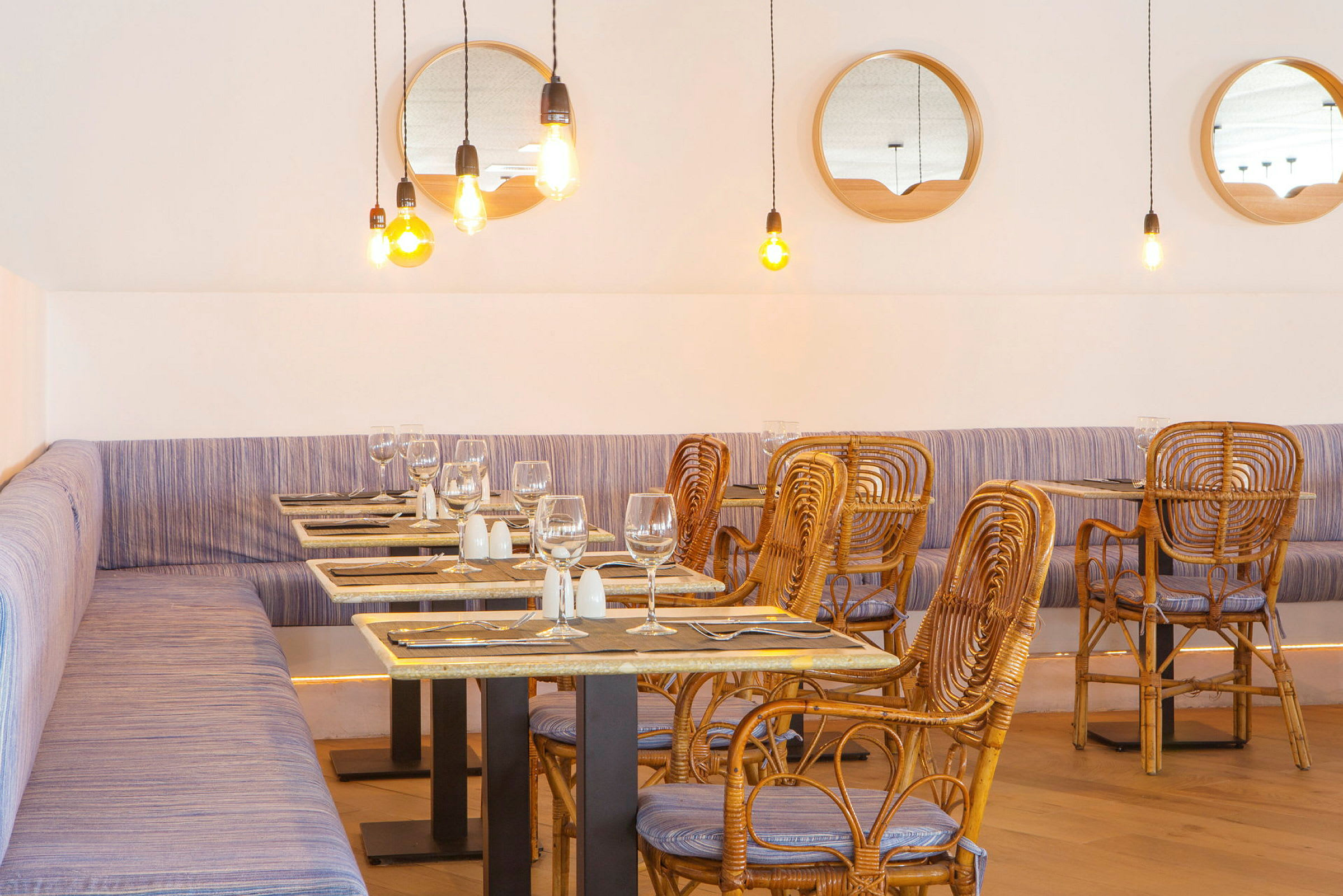 Restaurant med rottingstoler og bord, lyse hengende lamper og speil på veggen. (AI-generert tekst)