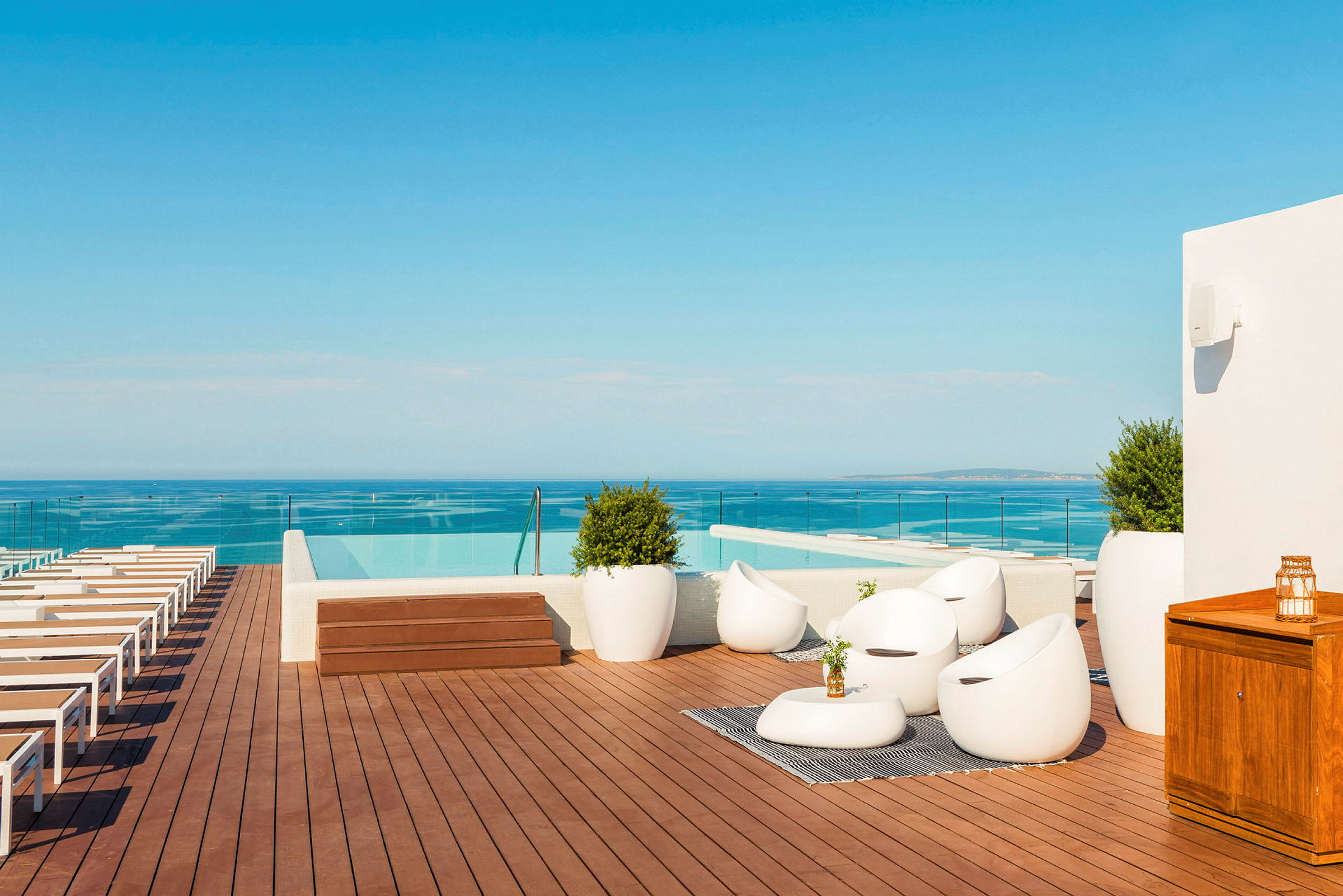 En takterrasse med solsenger, sittegruppe og infinitybasseng med utsikt over havet. (AI-generert tekst)