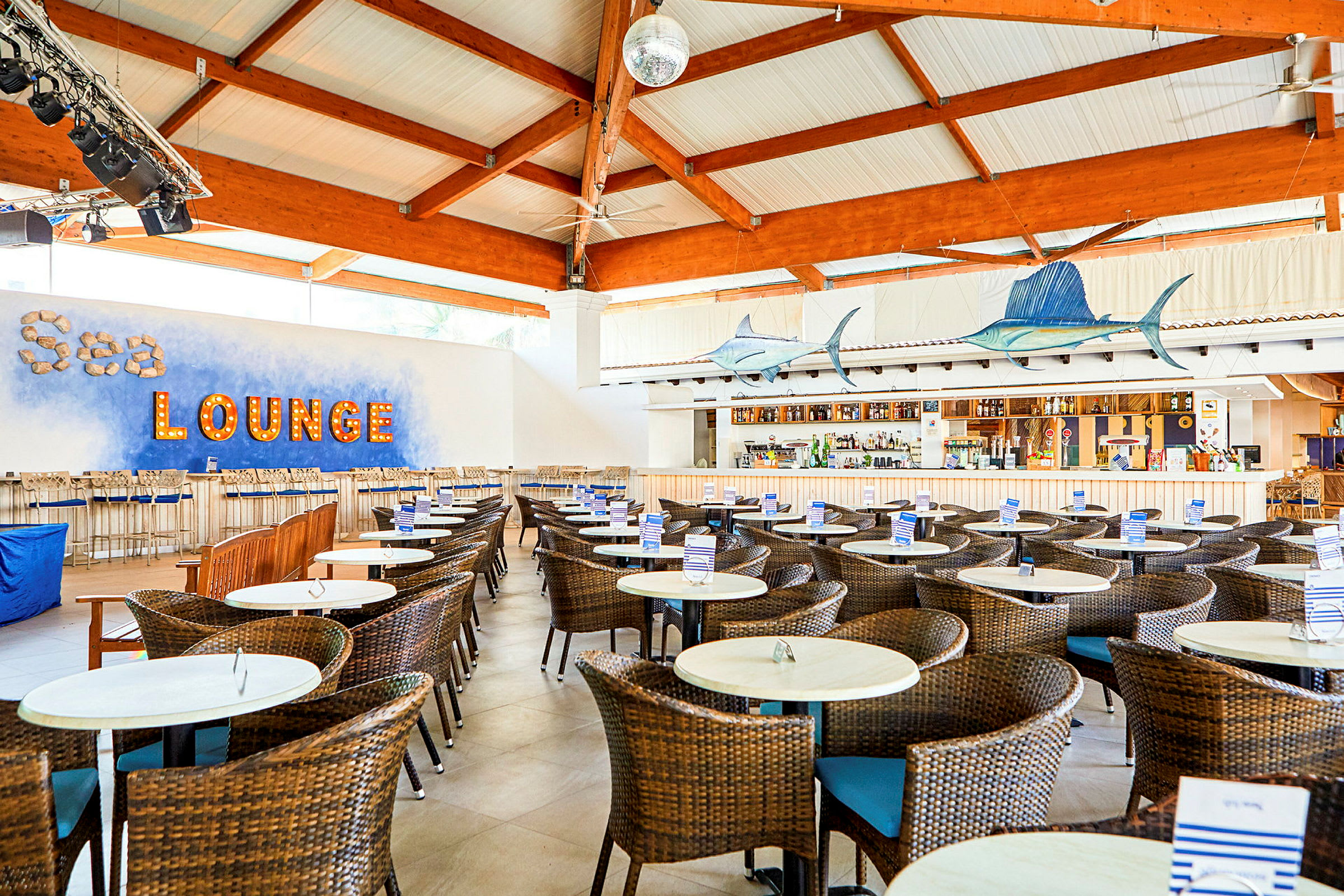 Interiør av en strandbar med rottingstoler og bord, opplyst tekst som lyder 'Sea lounge' på veggen. (AI-generert tekst)