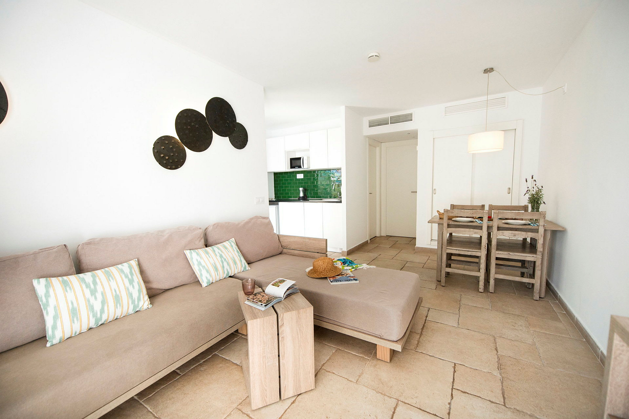 En moderne stue med en beige sofa, et trebord og en spiseplass ved siden av et lite kjøkken. (AI-generert tekst)