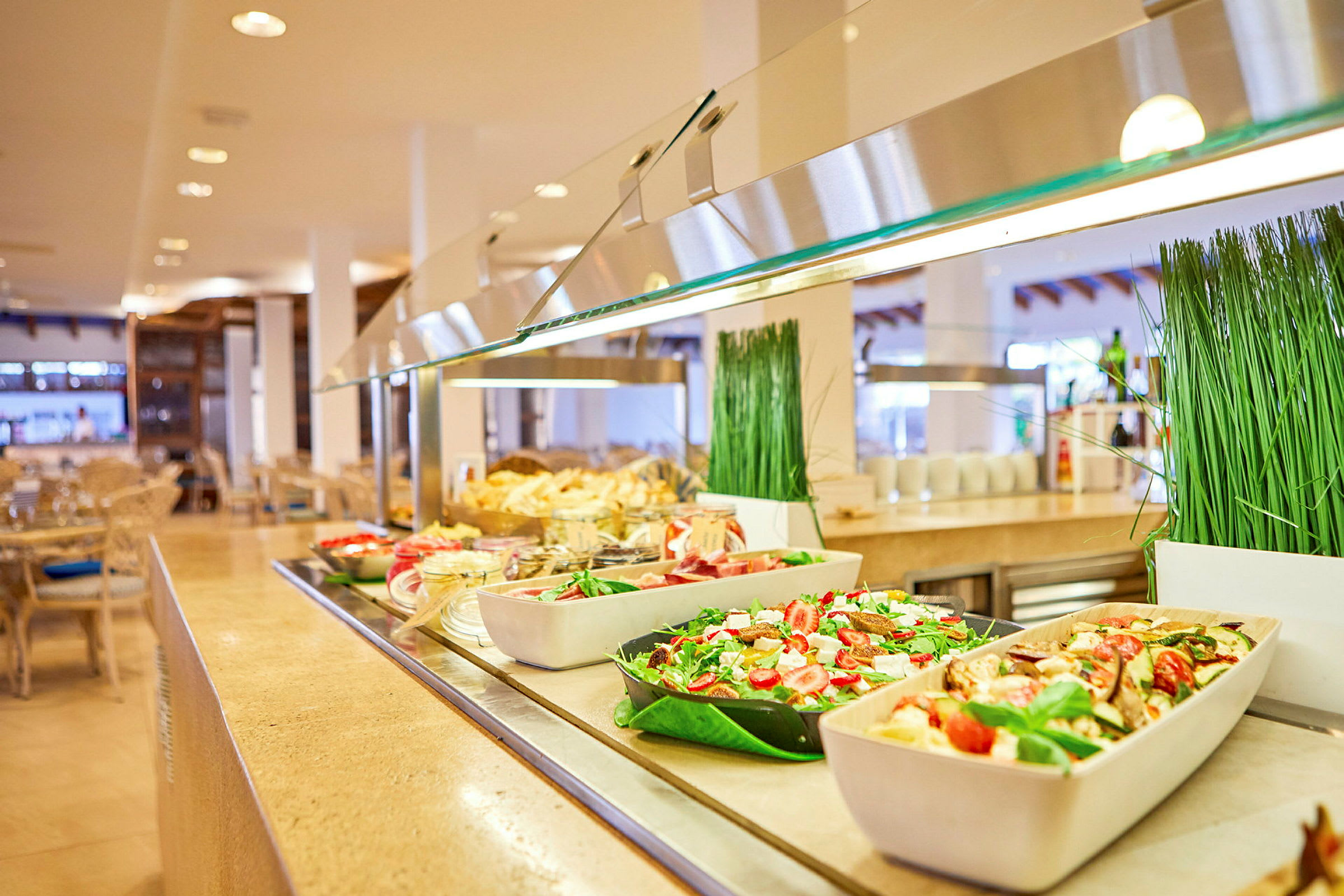 En buffet med forskjellige retter, inkludert salater og frukt, i en lys spisesal. (AI-generert tekst)