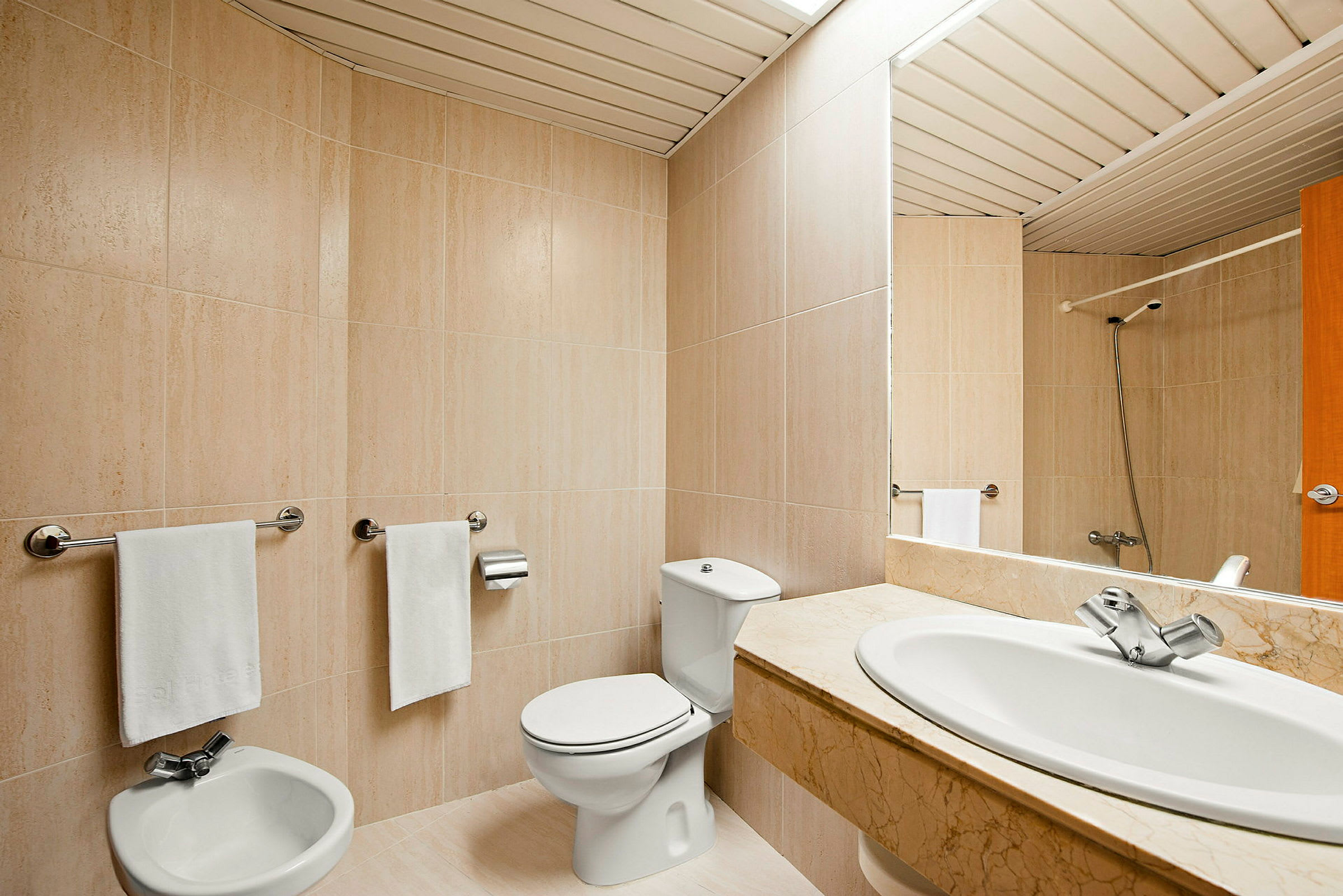 Et bad med beige flisevegger, toalett, bidet og en servant med marmorbord. (AI-generert tekst)