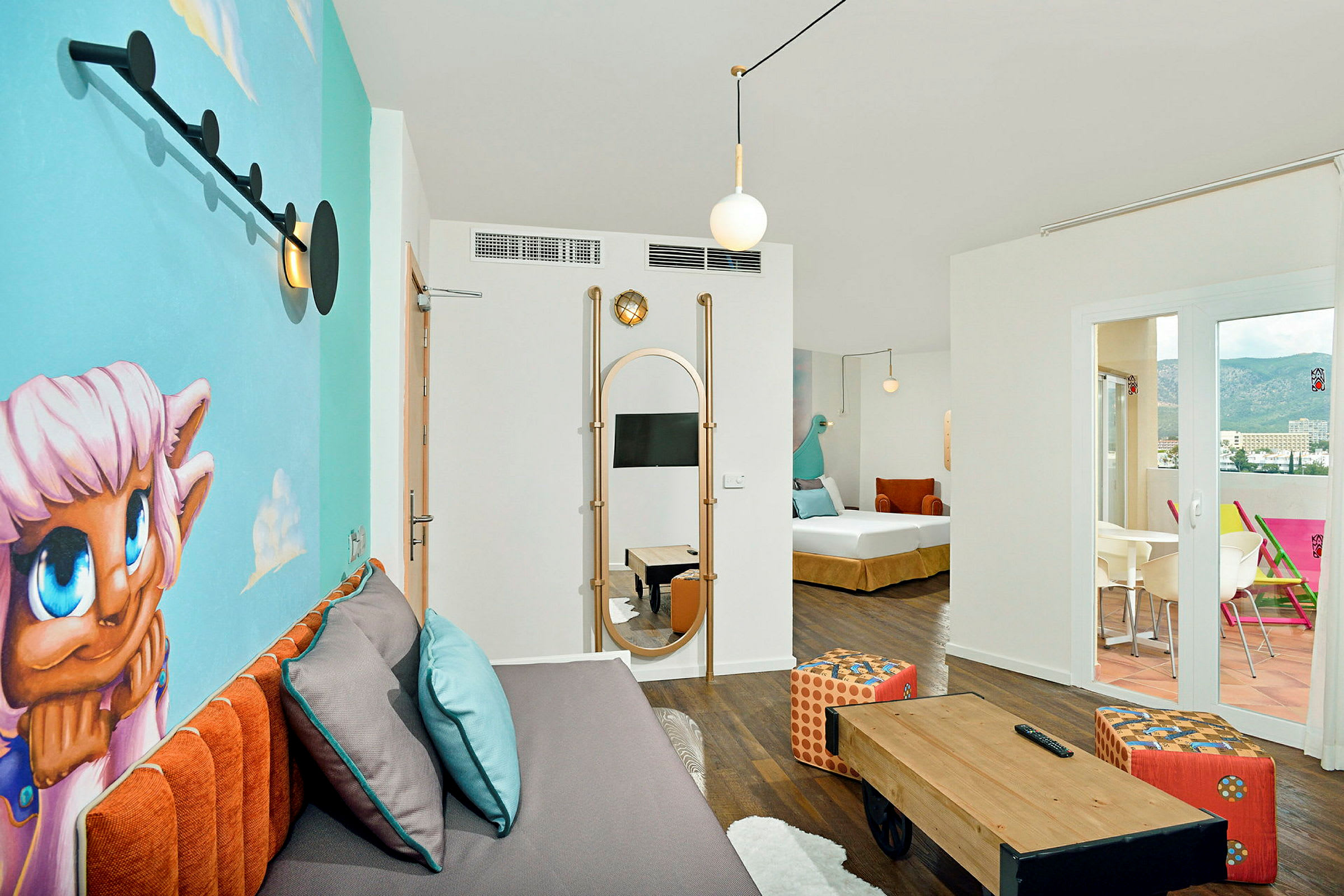 Et moderne og fargerikt hotellrom med en veggmaleri, en sofa med puter, et lite bord og en terrasse med utsikt. (AI-generert tekst)