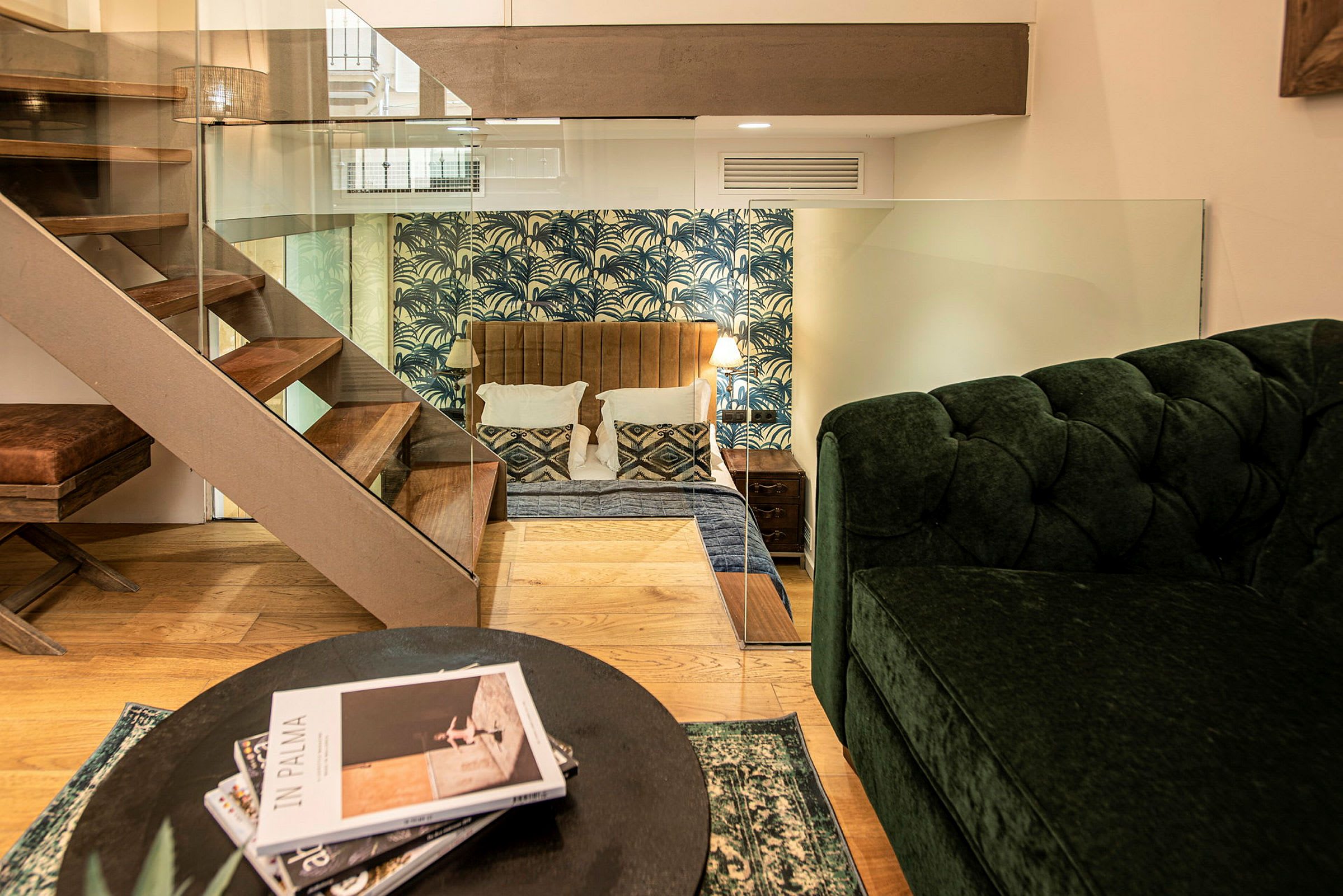 Interiøret i et hotellrom med soveområde og stue med grønn sofa og trapp. (AI-generert tekst)