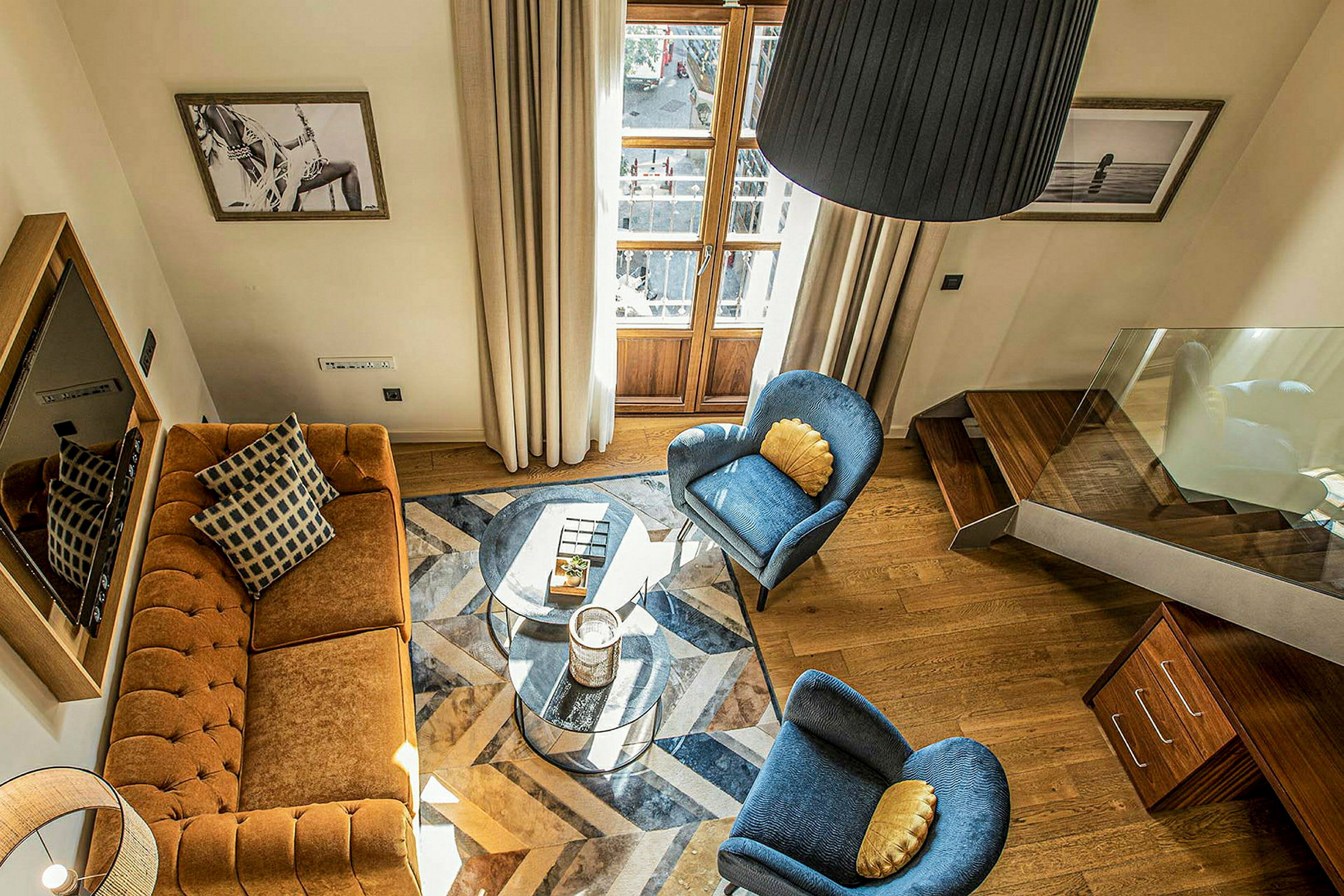 Et stue med en brun sofa, to blå stoler, et glassbord og tredetaljer. Bilder henger på veggene. (AI-generert tekst)