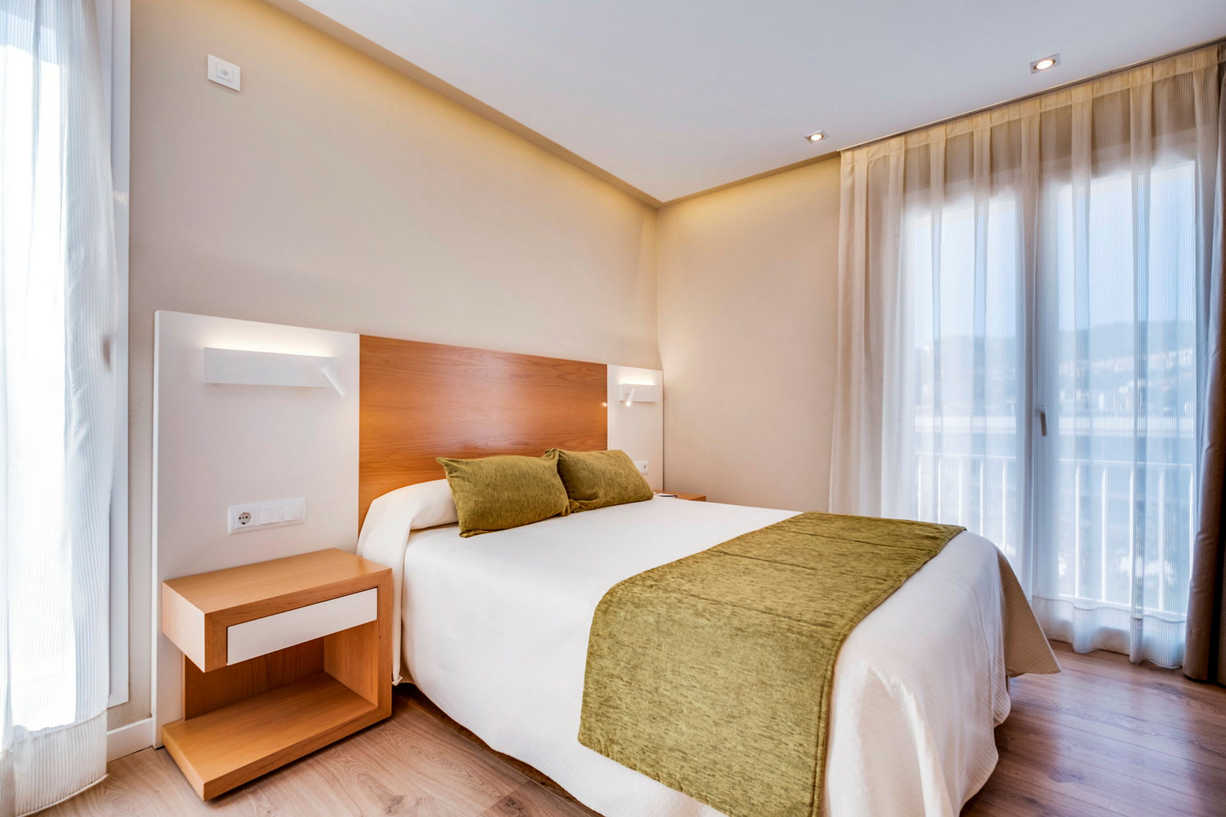 Et hotellrom med en dobbeltseng med grønne puter og sengeteppe. Et nattbord står ved siden av sengen. (AI-generert tekst)
