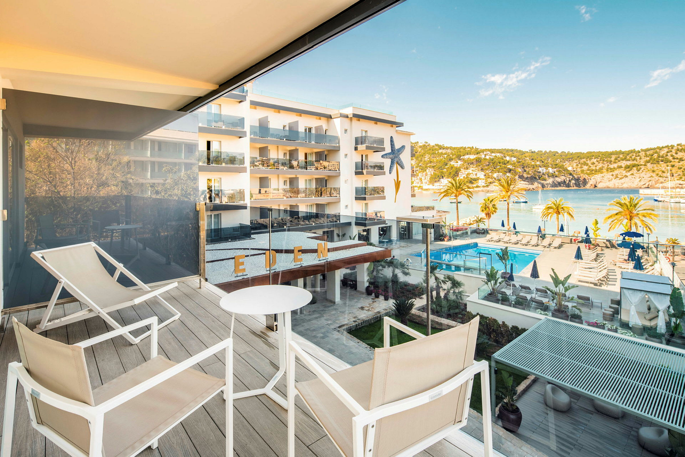 Utsikt fra en terrasse med sitteplasser, område med basseng og hav i bakgrunnen. (AI-generert tekst)