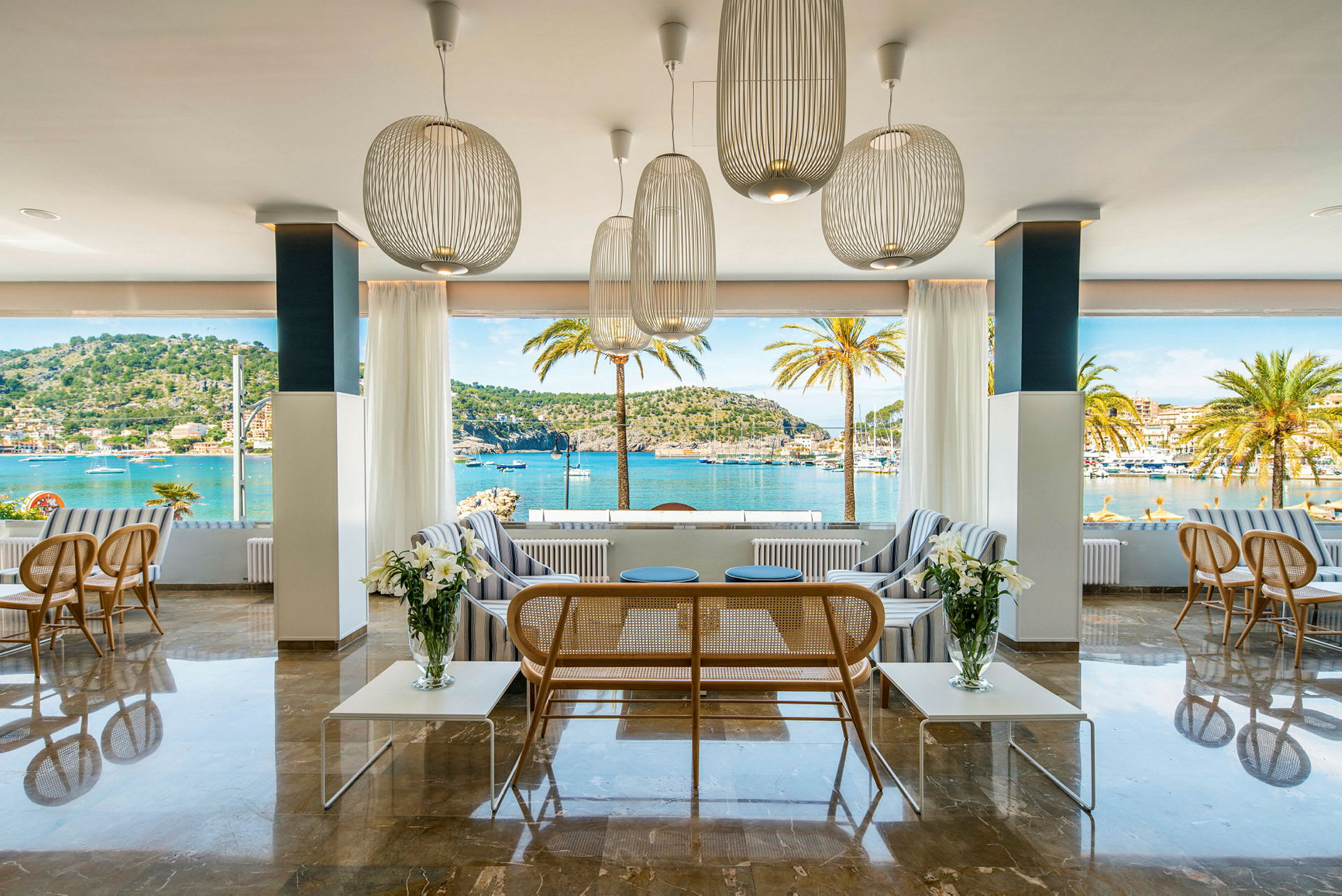 En elegant lounge med møbler og store vinduer som tilbyr utsikt over havet og palmer. (AI-generert tekst)