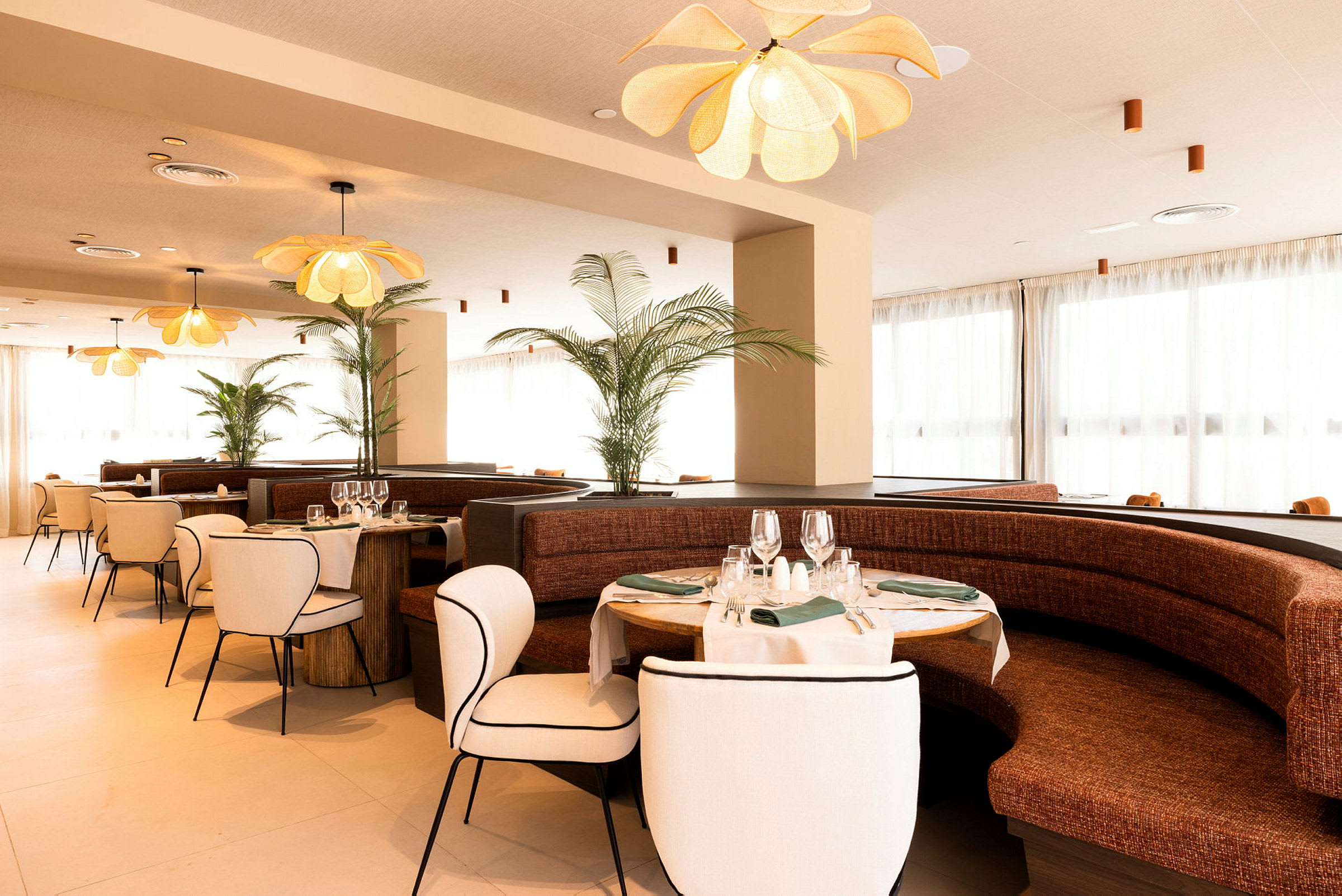 Restaurant med elegant interiør, bestående av runde bord med duker og vinglass samt komfortable stoler og sofaer. (AI-generert tekst)