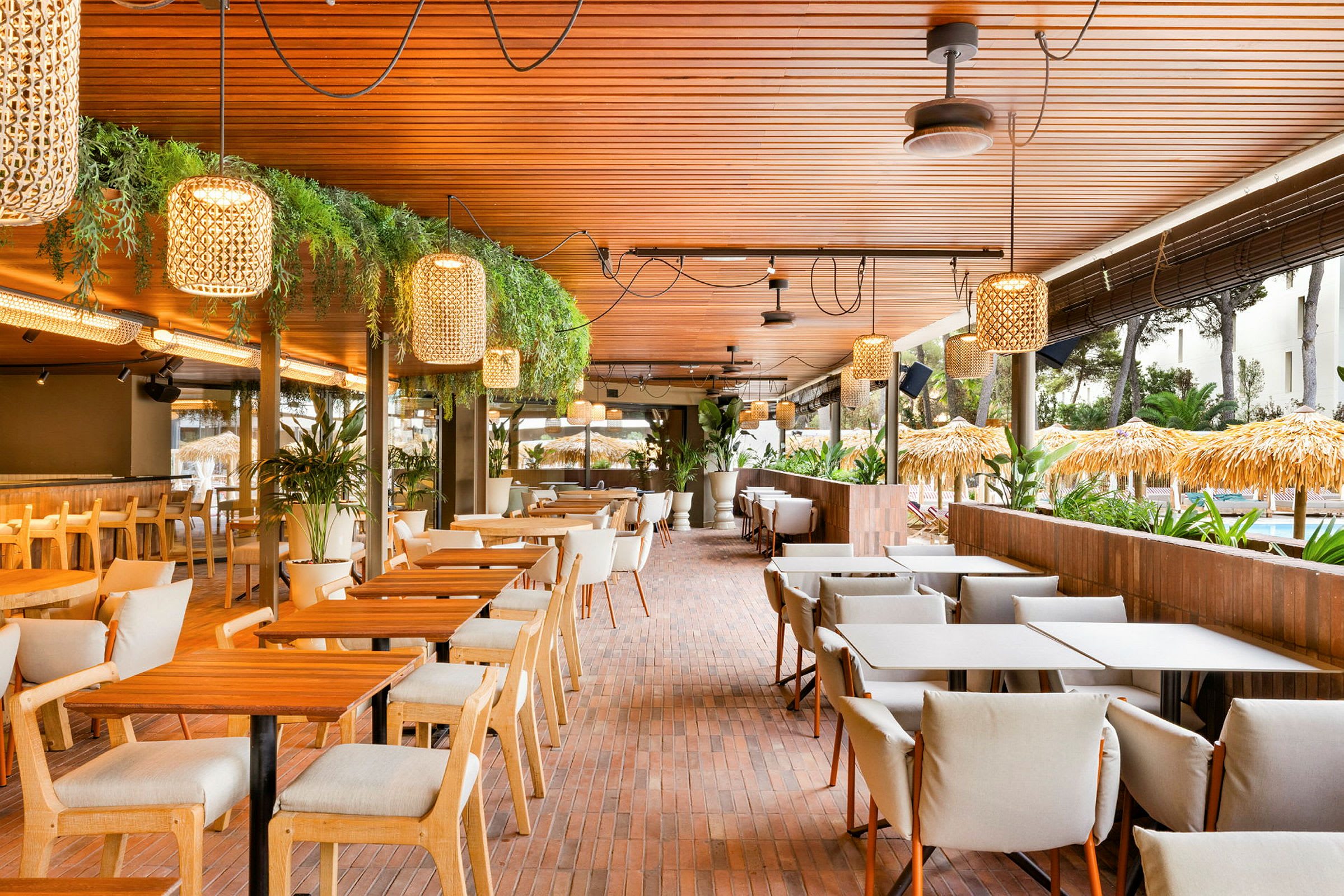 Bilde av en lys og moderne utendørsrestaurant med trebord, komfortable stoler og dekorative lamper. (AI-generert tekst)