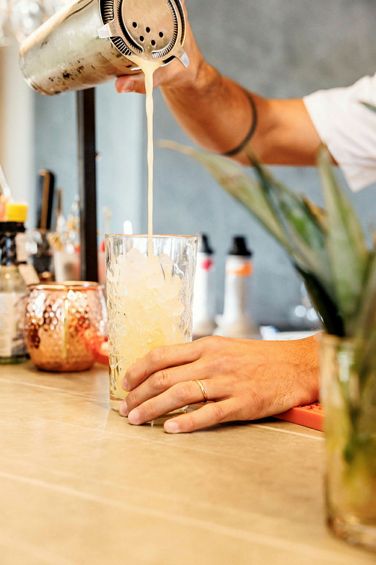 En person heller en drink fra en shaker ned i et glass fylt med is. (AI-generert tekst)