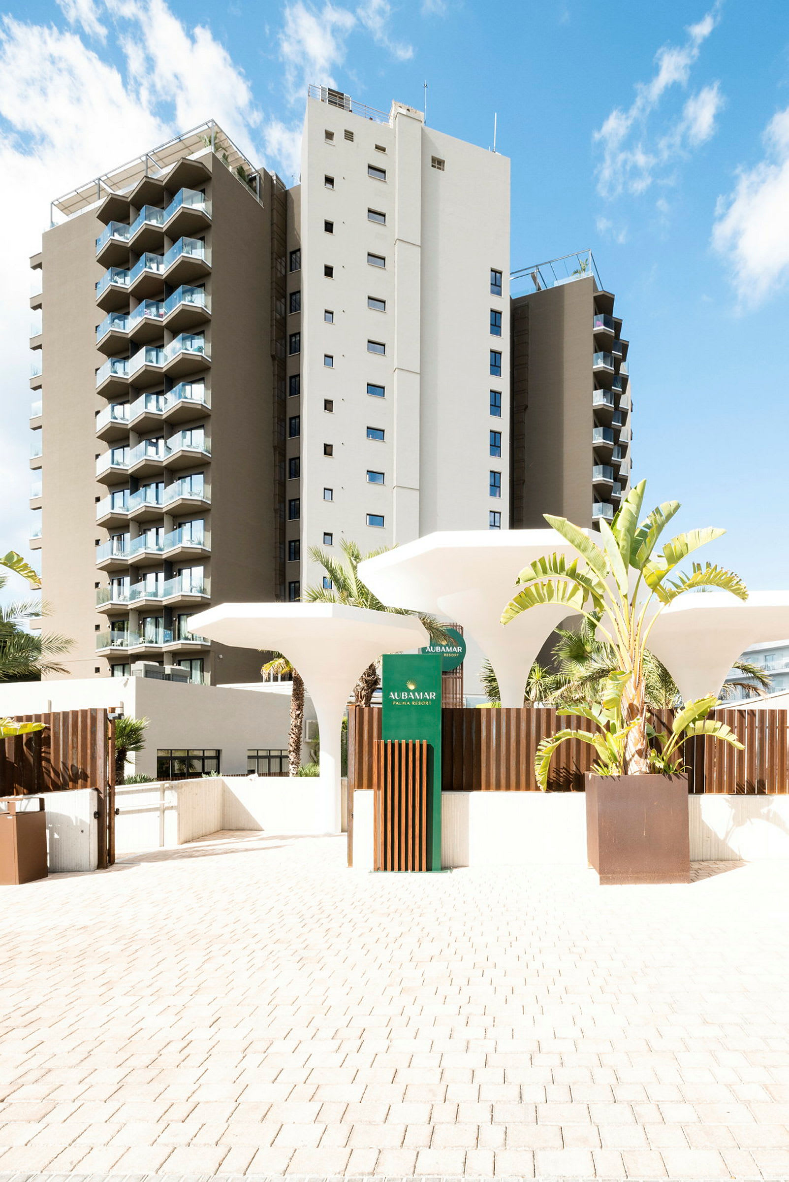 Et hotell i moderne design med hvite og beige fasader, flere balkonger og frodige planter ved inngangen. (AI-generert tekst)