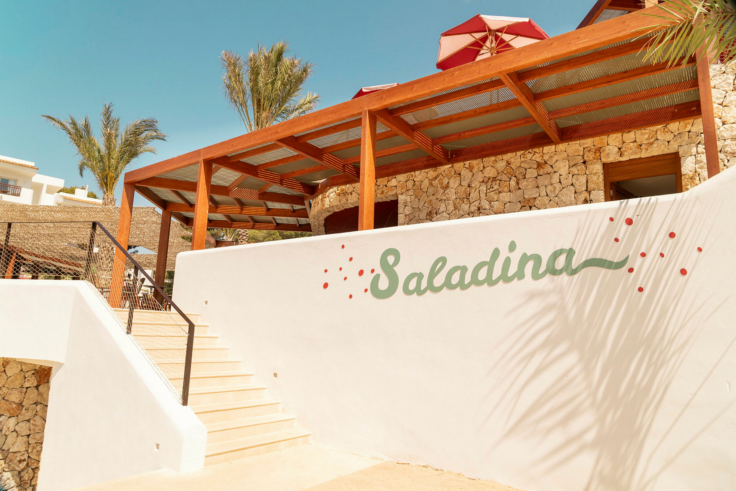 Hvit bygning med trapper, logoen "Saladina" på veggen og palmer i bakgrunnen. (AI-generert tekst)