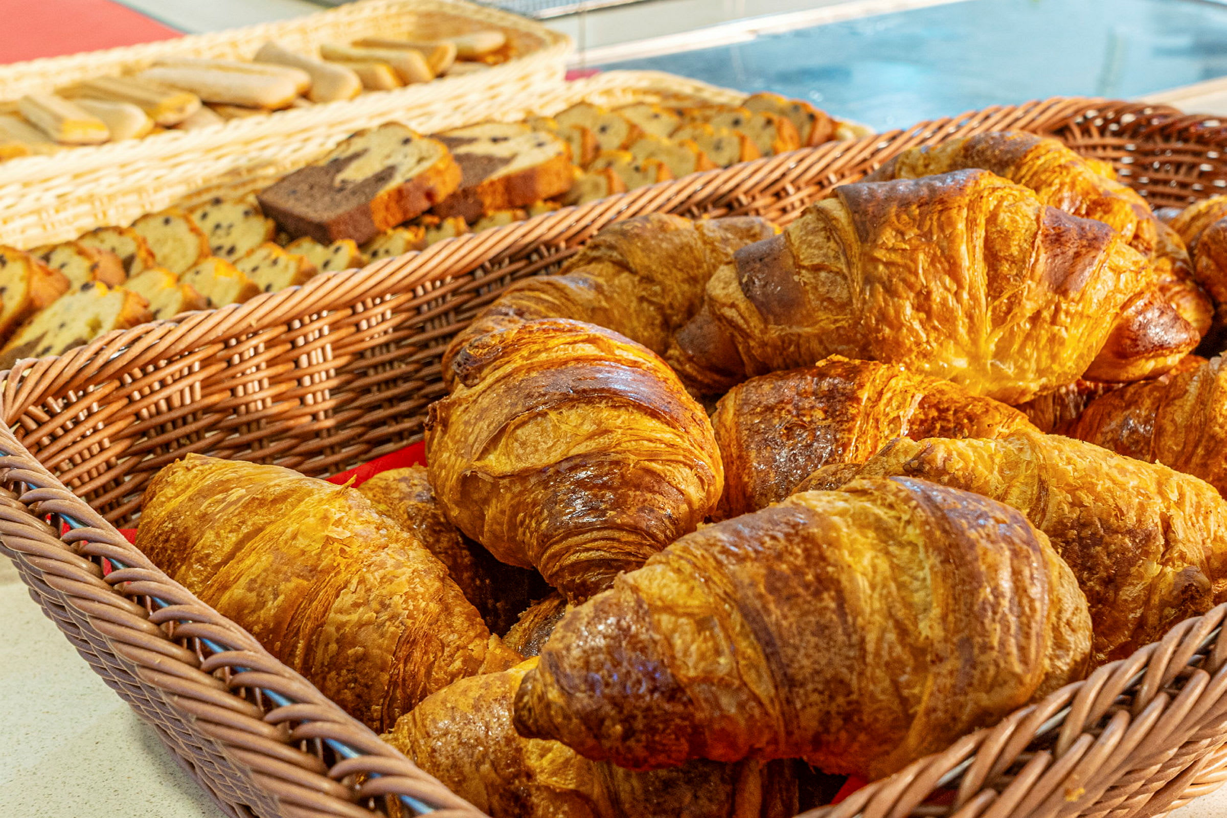 En kurv med croissanter foran en bakgrunn med ulike bakverk. (AI-generert tekst)