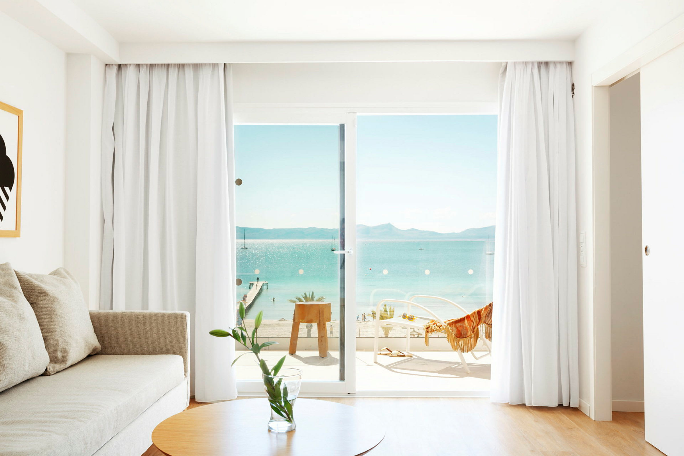 Bilde av et lyst rom med en sofa, et bord og glassdører som leder til en balkong med utsikt over havet. (AI-generert tekst)