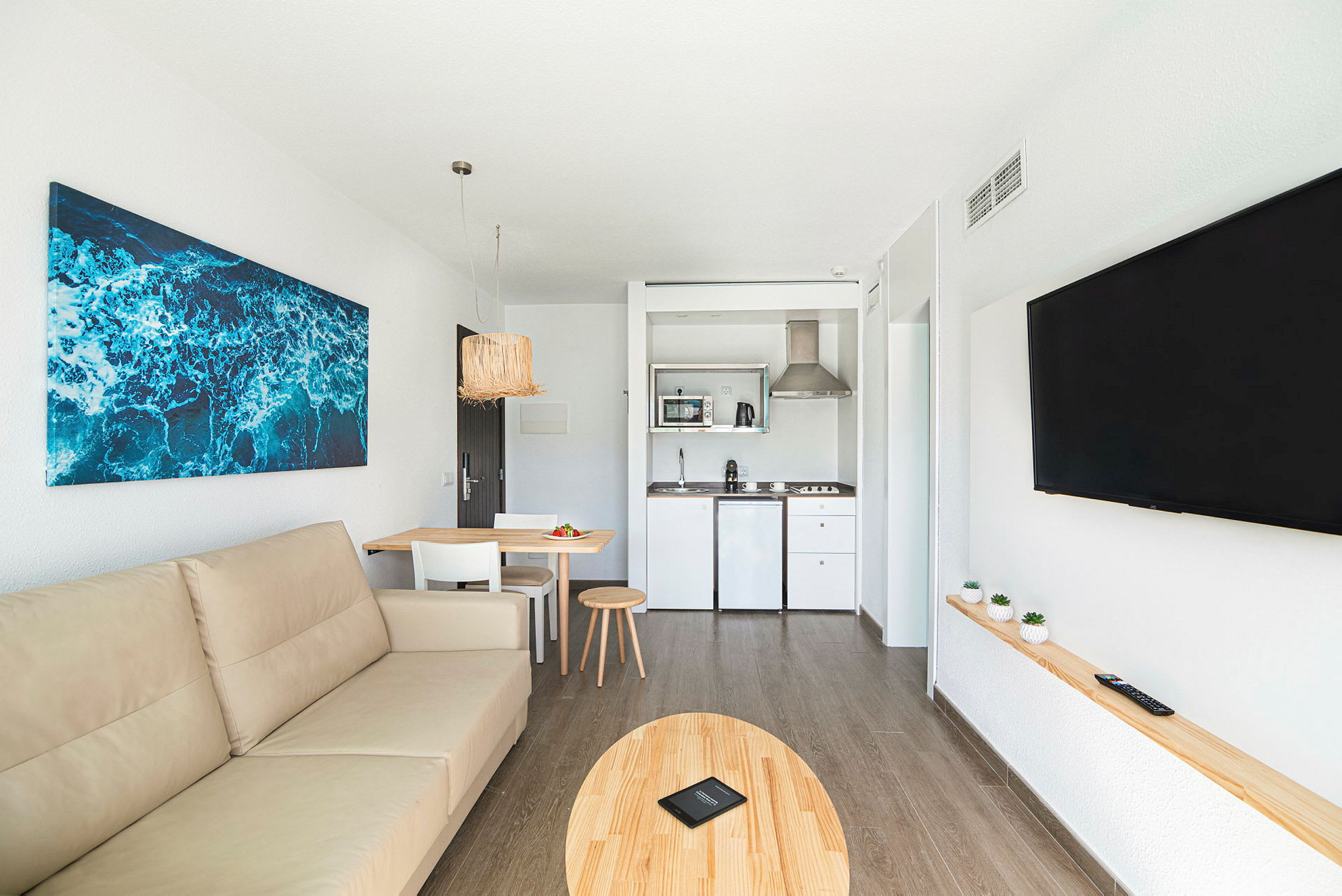 Et stue med en beige sofa, et spisebord og et kjøkken i bakgrunnen. (AI-generert tekst)