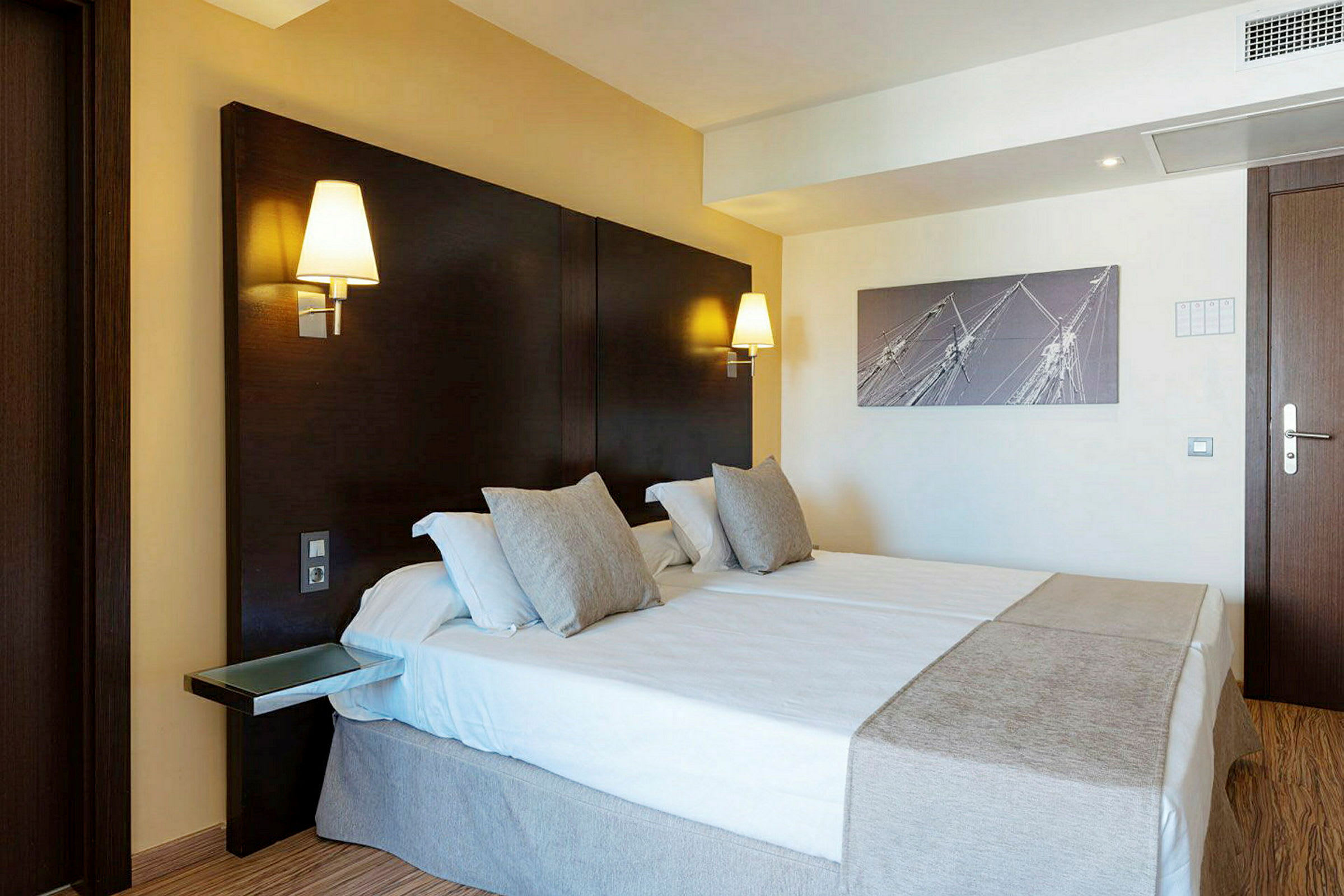Et hotellrom med en dobbeltseng, veggmonterte lamper og en moderne innredning. (AI-generert tekst)