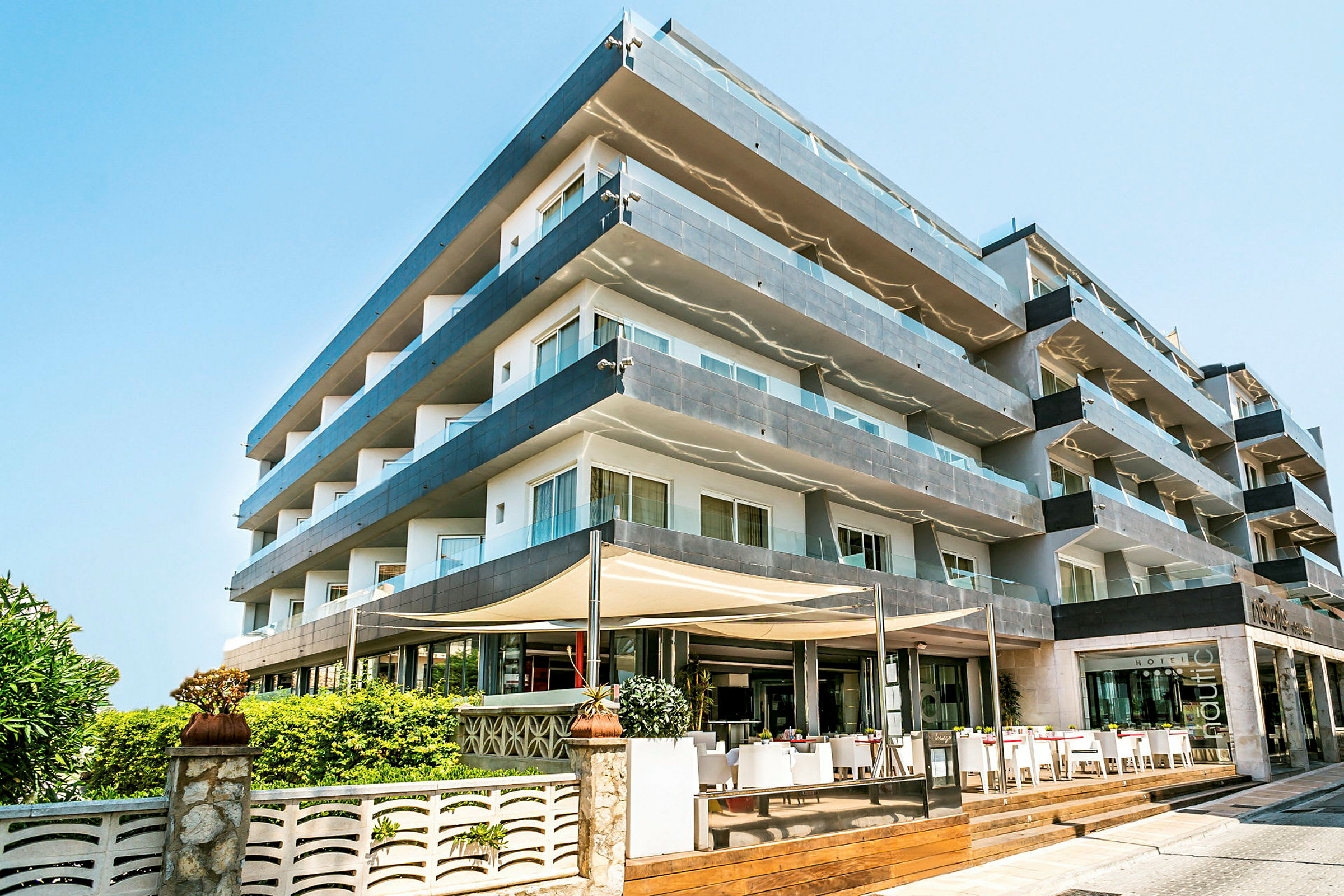 Bilde av et fleretagers hotell med glassbalkonger og en inngang med uteservering. (AI-generert tekst)